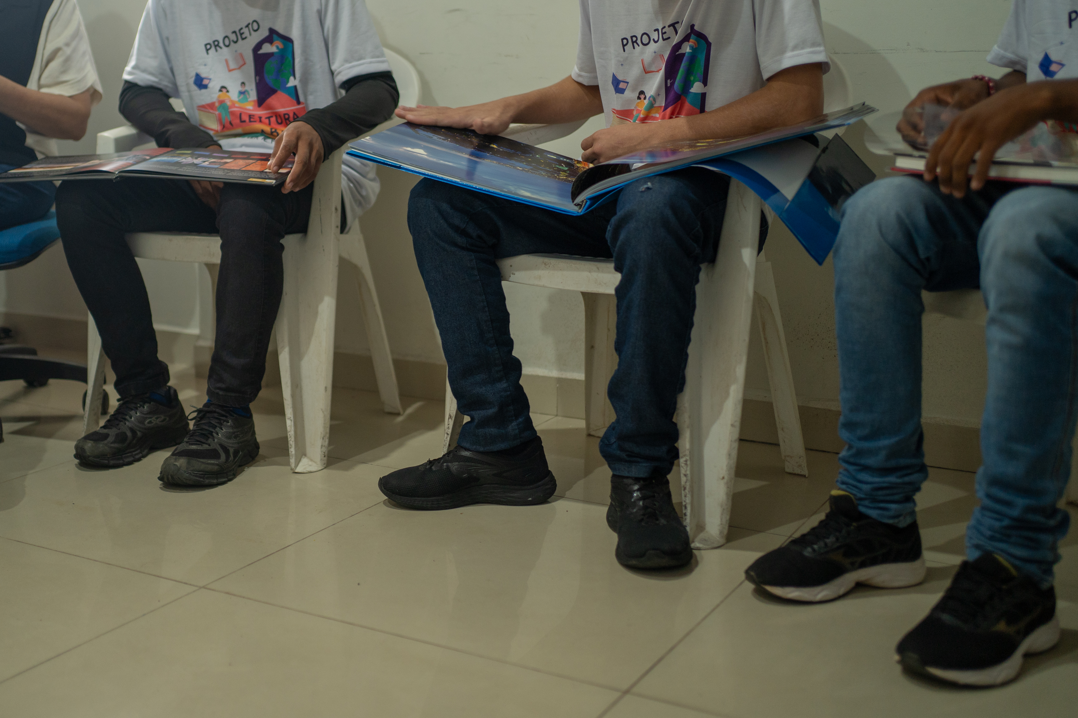 Foto colorida exibe jovens e adolescentes sem mostrar rosto e identidade deles, sentados, durante oficina de fotografia Foto colorida exibe jovens e adolescentes sem mostrar rosto e identidade deles, sentados, durante oficina de fotografia