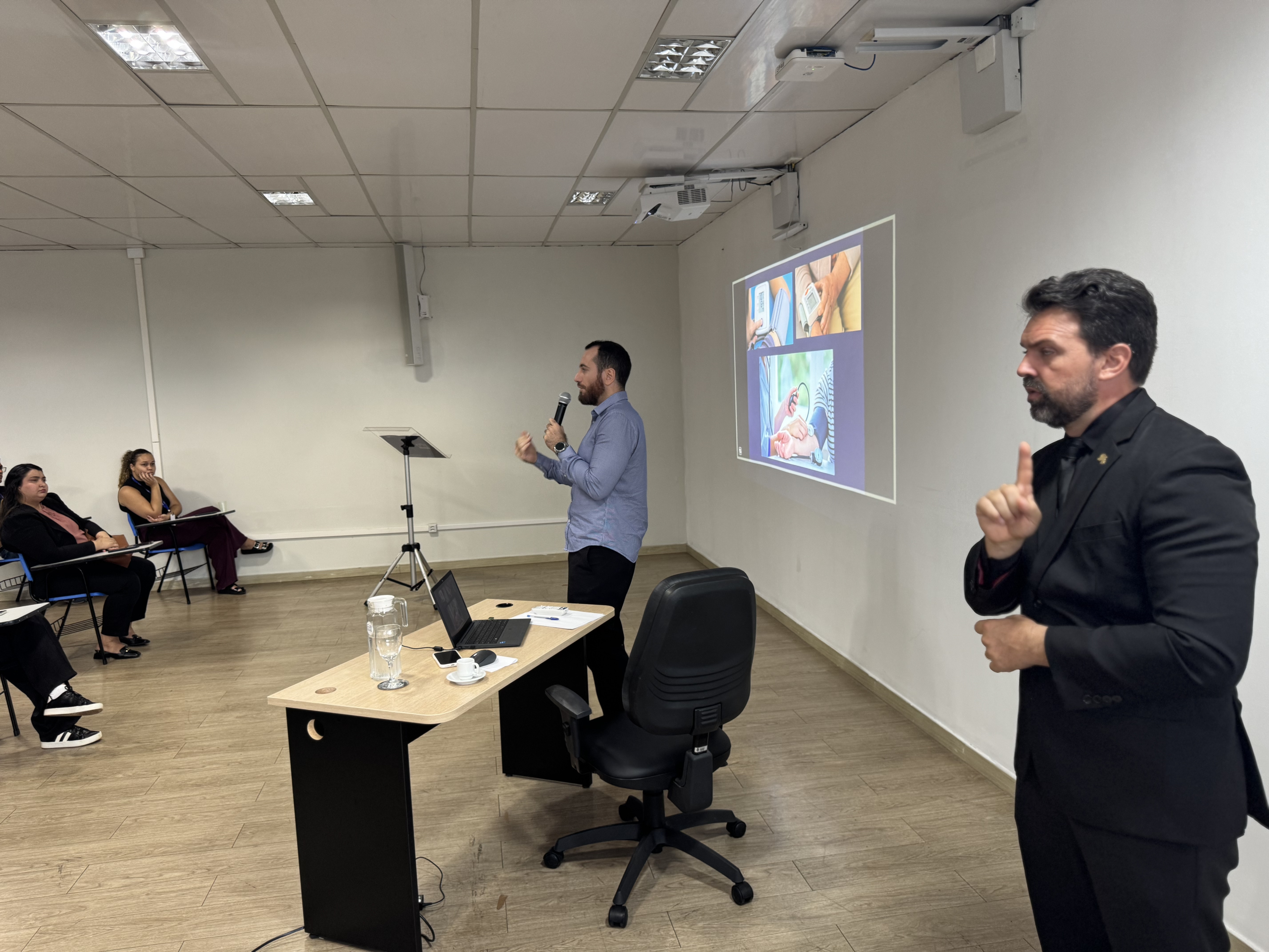 Foto 2: A imagem mostra o secretário de Qualidade de Vida, Dr. Hassan Syagha, palestrando para integrantes do Judiciário roraimense, que estão sentados em filas de cadeiras e ao lado há um interprete de libras. O tema abordado é a hipertensão arterial sistêmica, incluindo formas de prevenção, diagnóstico e tratamento da doença. Ao fundo, é possível ver uma apresentação de PowerPoint projetada na parede, com a pergunta: “Preciso tomar remédio para o resto da vida?” Foto 2: A imagem mostra o secretário de Qualidade de Vida, Dr. Hassan Syagha, palestrando para integrantes do Judiciário roraimense, que estão sentados em filas de cadeiras e ao lado há um interprete de libras. O tema abordado é a hipertensão arterial sistêmica, incluindo formas de prevenção, diagnóstico e tratamento da doença. Ao fundo, é possível ver uma apresentação de PowerPoint projetada na parede, com a pergunta: “Preciso tomar remédio para o resto da vida?”