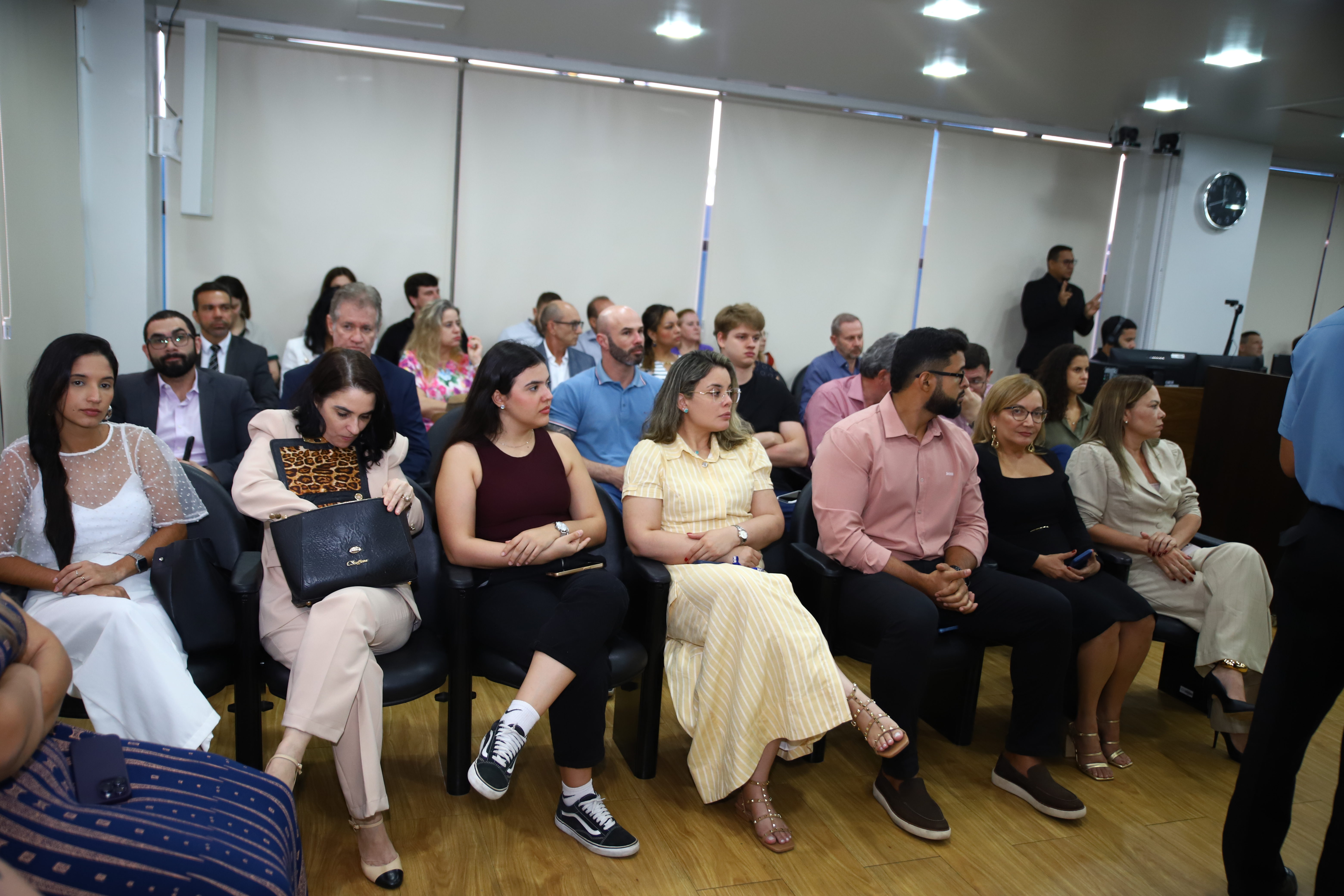 Foto colorida da plateia. Ao fundo da para ver um intérprete de Libras Foto colorida da plateia. Ao fundo da para ver um intérprete de Libras