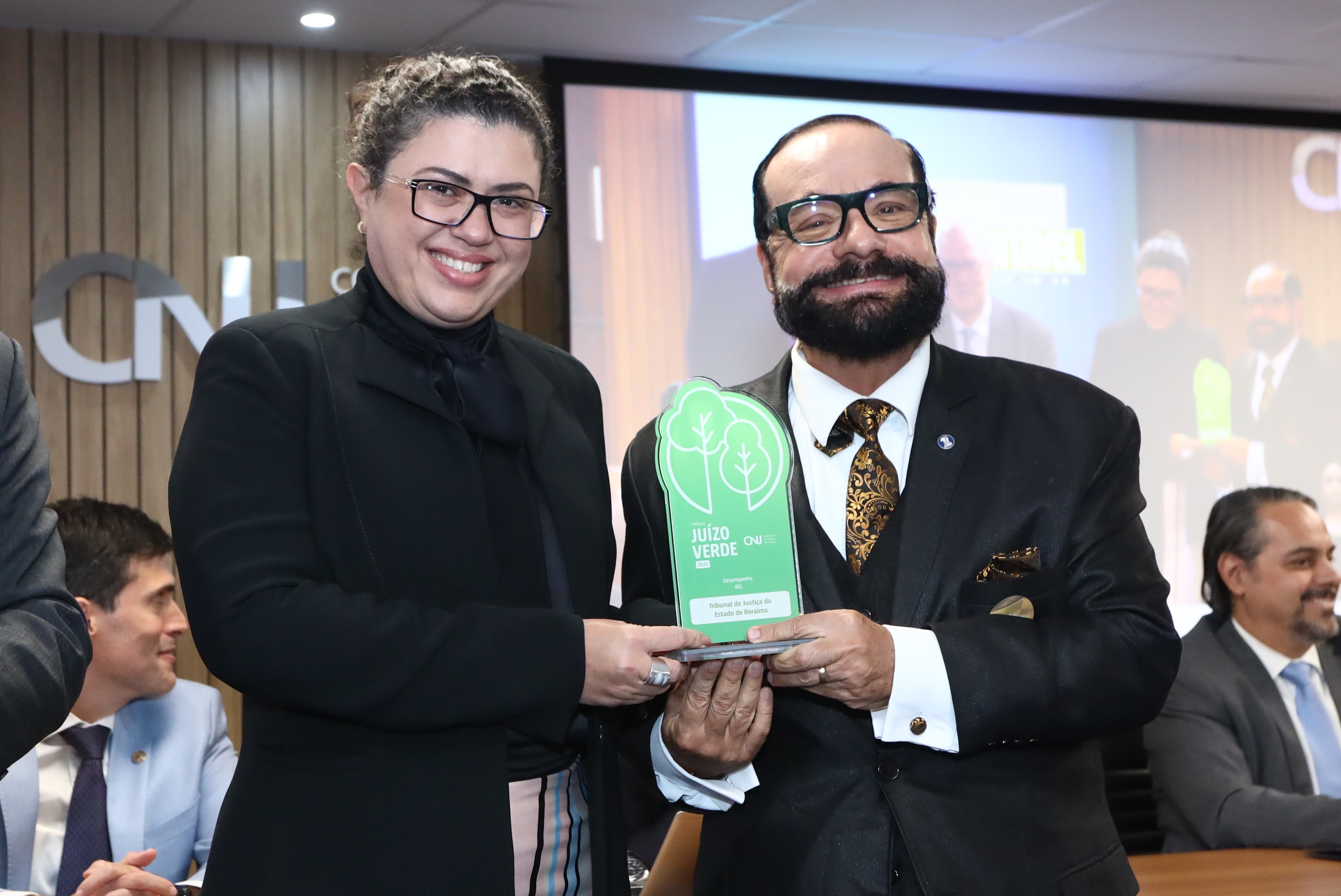 Imagem colorida do presidente do TJRR, desembargador Leonardo Cupello, ao lado de uma mulher segurando o prêmio e pousando para fotografia. Imagem colorida do presidente do TJRR, desembargador Leonardo Cupello, ao lado de uma mulher segurando o prêmio e pousando para fotografia.