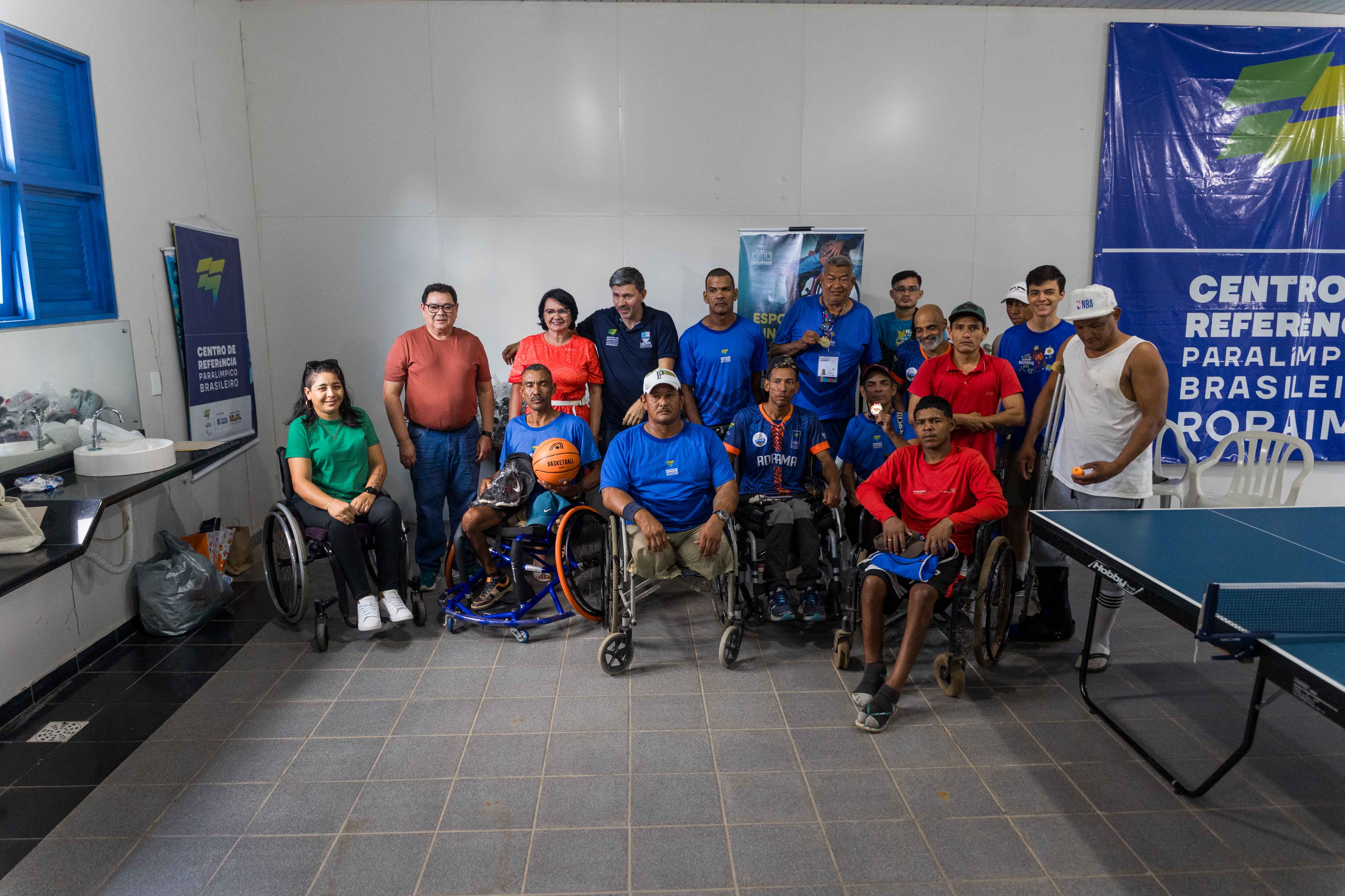 Foto colorida dividida ao meio mostra detalhes das pernas de dois atletas paralímpicos sentados em cadeiras de rodas esportivas azuladas. À esquerda, o atleta está descalço com uma bola de basquete no colo. À direita, o outro atleta usa tênis e boné, também com uma bola no colo. Foto colorida dividida ao meio mostra detalhes das pernas de dois atletas paralímpicos sentados em cadeiras de rodas esportivas azuladas. À esquerda, o atleta está descalço com uma bola de basquete no colo. À direita, o outro atleta usa tênis e boné, também com uma bola no colo.
