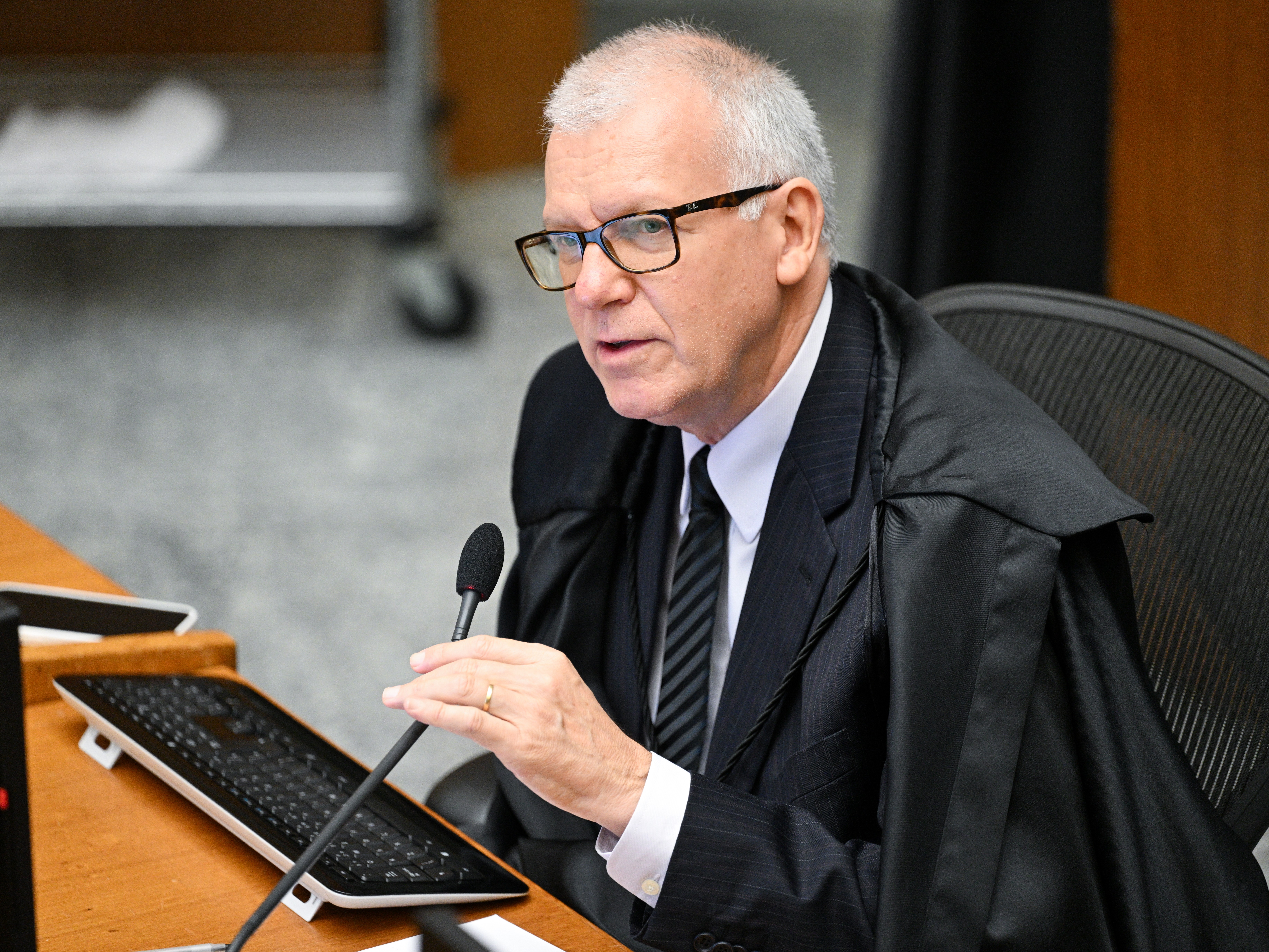 Foto colorida mostra o ministro do Superior Tribunal de Justiça (STJ) Sérgio Kukina, um homem branco, de cabelos curtos e grisalhos, usando óculos retangulares com armação escura, terno preto risca de giz, camisa branca e gravata listrada. Ele veste toga preta sobre o terno e está sentado à frente de um microfone. Foto colorida mostra o ministro do Superior Tribunal de Justiça (STJ) Sérgio Kukina, um homem branco, de cabelos curtos e grisalhos, usando óculos retangulares com armação escura, terno preto risca de giz, camisa branca e gravata listrada. Ele veste toga preta sobre o terno e está sentado à frente de um microfone.