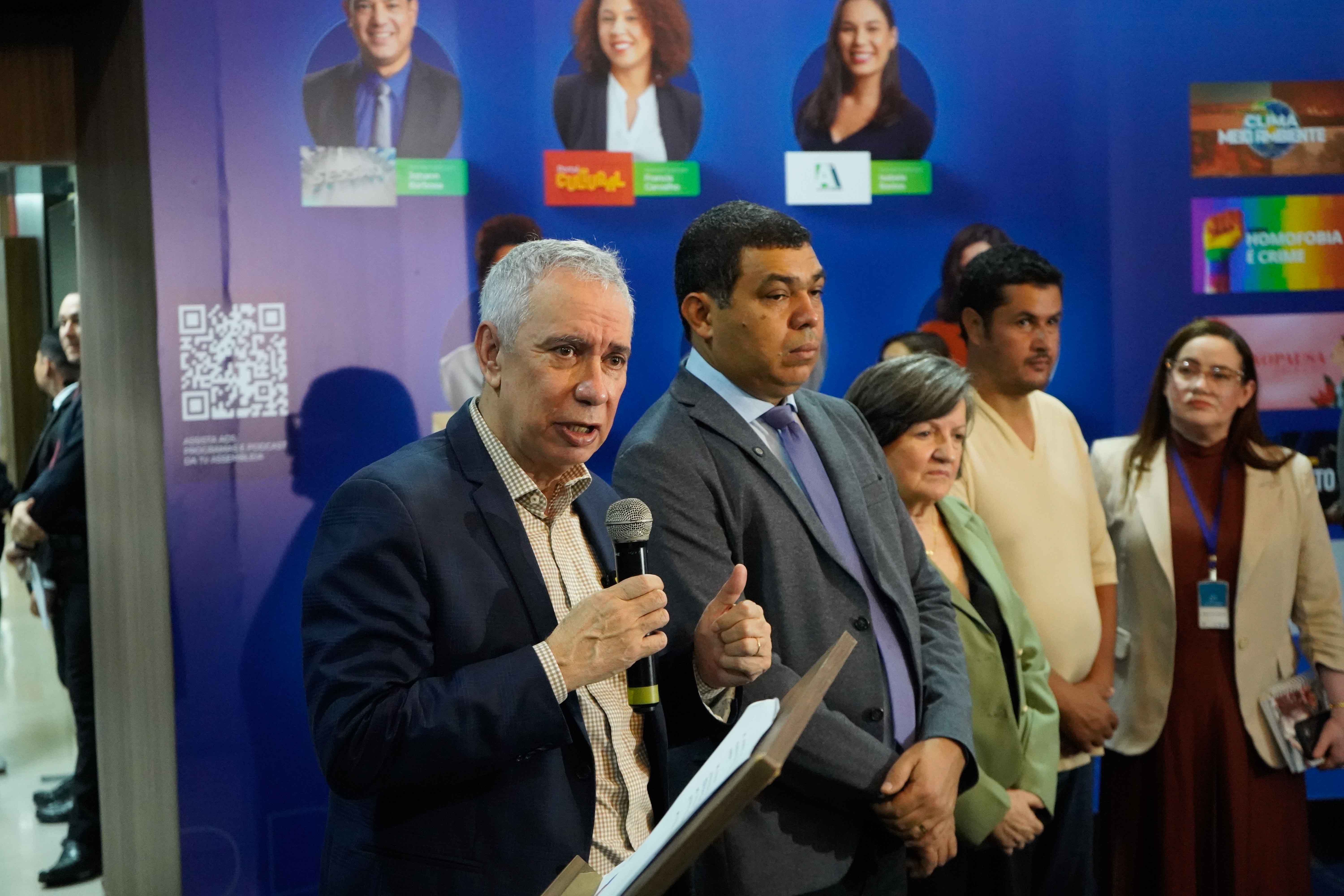 Imagem colorida mostra o Vice-Presidente do Tribunal de Justiça de Roraima, desembargador Almiro Padilha falando no microfone enquanto segura um papel em um púlpito. Ao seu lado, um homem mais jovem de terno cinza faz um gesto com o polegar para cima. Há outras pessoas atrás e ao lado deles. Imagem colorida mostra o Vice-Presidente do Tribunal de Justiça de Roraima, desembargador Almiro Padilha falando no microfone enquanto segura um papel em um púlpito. Ao seu lado, um homem mais jovem de terno cinza faz um gesto com o polegar para cima. Há outras pessoas atrás e ao lado deles.
