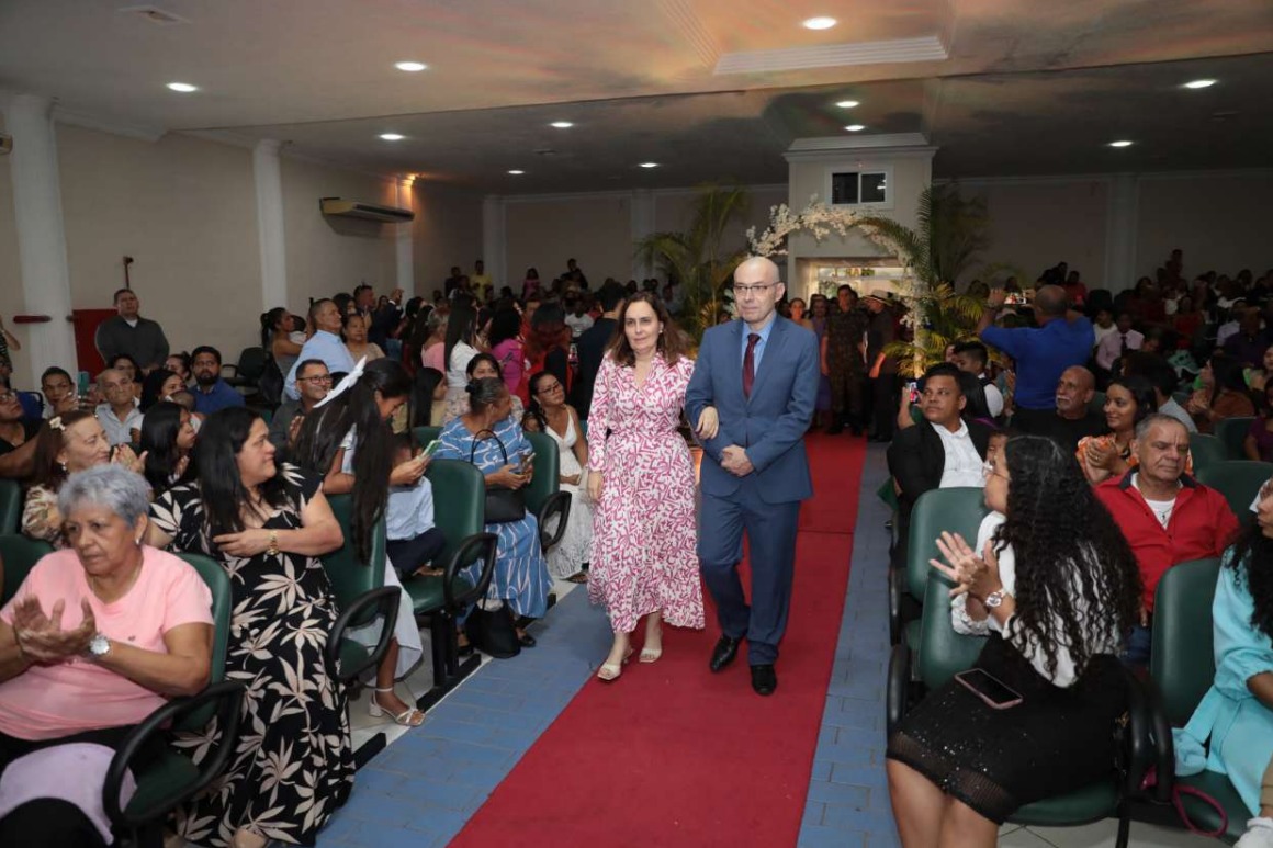 Foto colorida mostra o desembargador Erick Linhares, corregedor-geral de justiça do TJRR, caminhando de braços dados com sua esposa, por um corredor com tapete vermelho em um auditório lotado. Foto colorida mostra o desembargador Erick Linhares, corregedor-geral de justiça do TJRR, caminhando de braços dados com sua esposa, por um corredor com tapete vermelho em um auditório lotado.