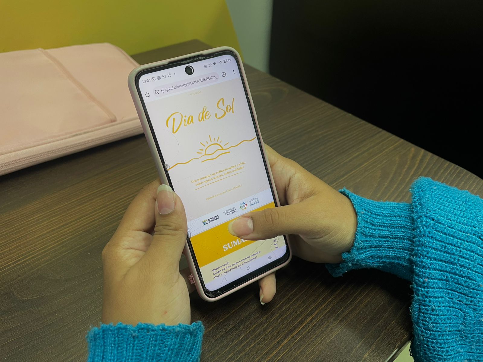 Imagem colorida dando enfoque na mão de uma mulher segurando o celular com a pagina do e-book aberta. Imagem colorida dando enfoque na mão de uma mulher segurando o celular com a pagina do e-book aberta.