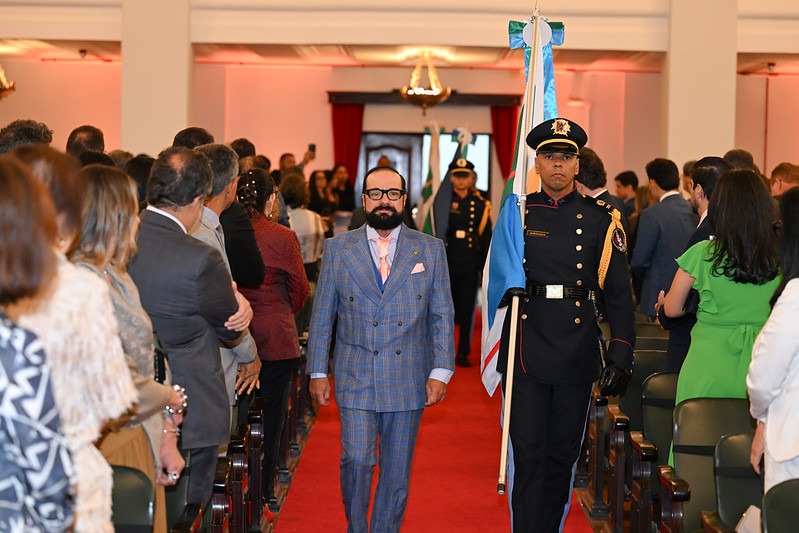 Foto colorida do presidente do TJRR, desembargador Leonardo Cupello, caminhando em um tapete vermelho, acompanhado por um militar que carrega uma bandeira, em cerimônia da abertura do evento com público dos dois lados. Foto colorida do presidente do TJRR, desembargador Leonardo Cupello, caminhando em um tapete vermelho, acompanhado por um militar que carrega uma bandeira, em cerimônia da abertura do evento com público dos dois lados.