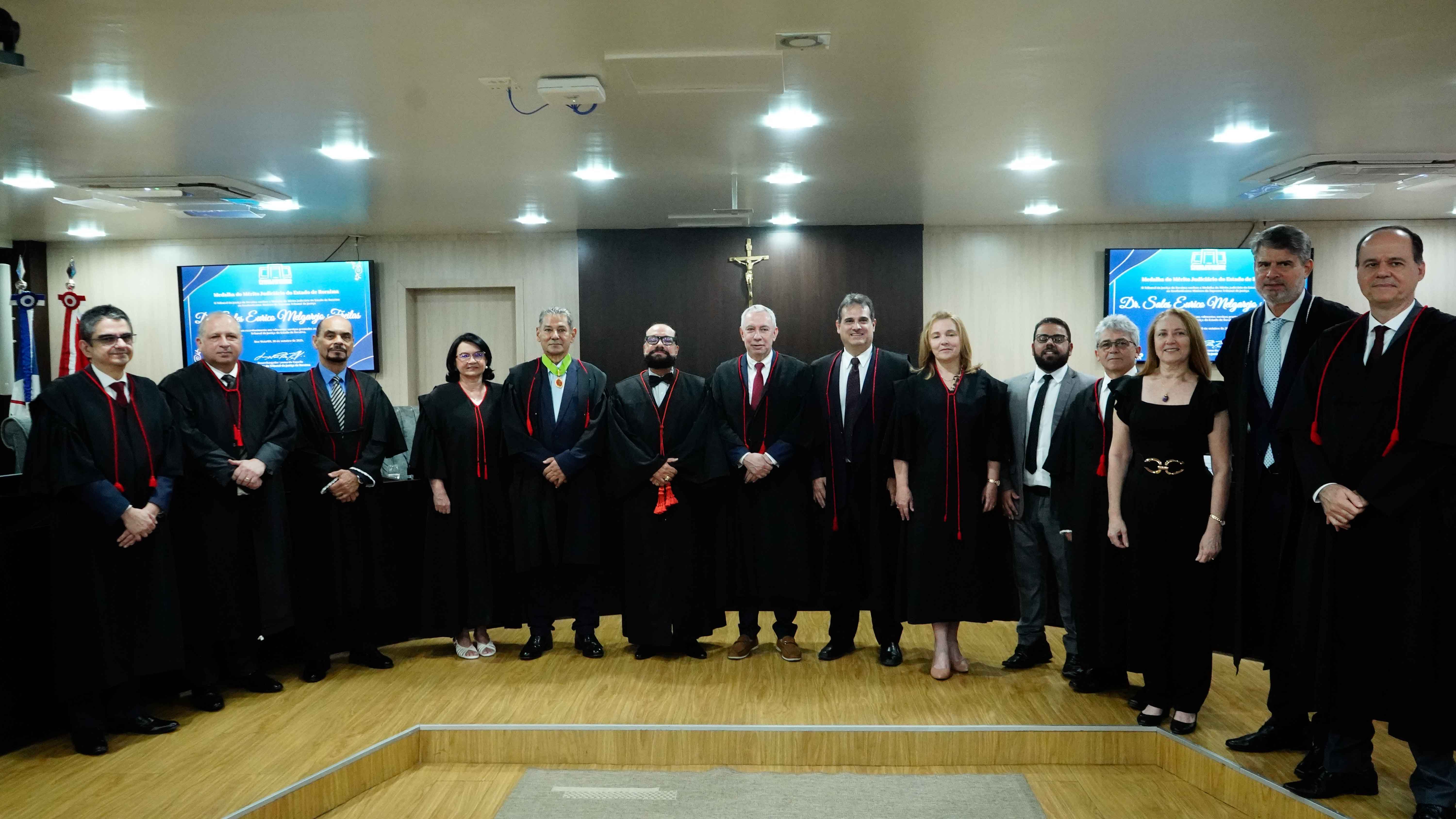 Imagem colorida mostra grupo de autoridades posa para foto oficial em um plenário. O Desembargador Leonardo Cupello e o Procurador Sales Eurico Melgarejo Freitas, usando a comenda, estão entre os presentes, a maioria vestindo togas pretas e alinhados em frente à bancada de madeira.  Imagem colorida mostra grupo de autoridades posa para foto oficial em um plenário. O Desembargador Leonardo Cupello e o Procurador Sales Eurico Melgarejo Freitas, usando a comenda, estão entre os presentes, a maioria vestindo togas pretas e alinhados em frente à bancada de madeira.