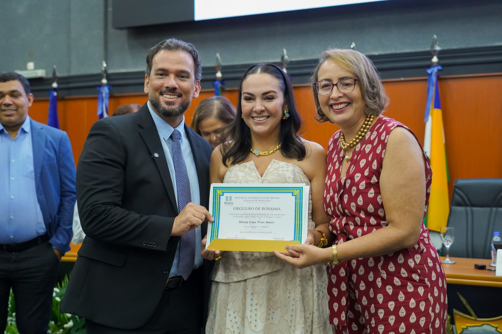 Foto 1: Imagem colorida de três pessoas posando para fotografia com o certificado em mãos durante a solenidade. Foto 1: Imagem colorida de três pessoas posando para fotografia com o certificado em mãos durante a solenidade.