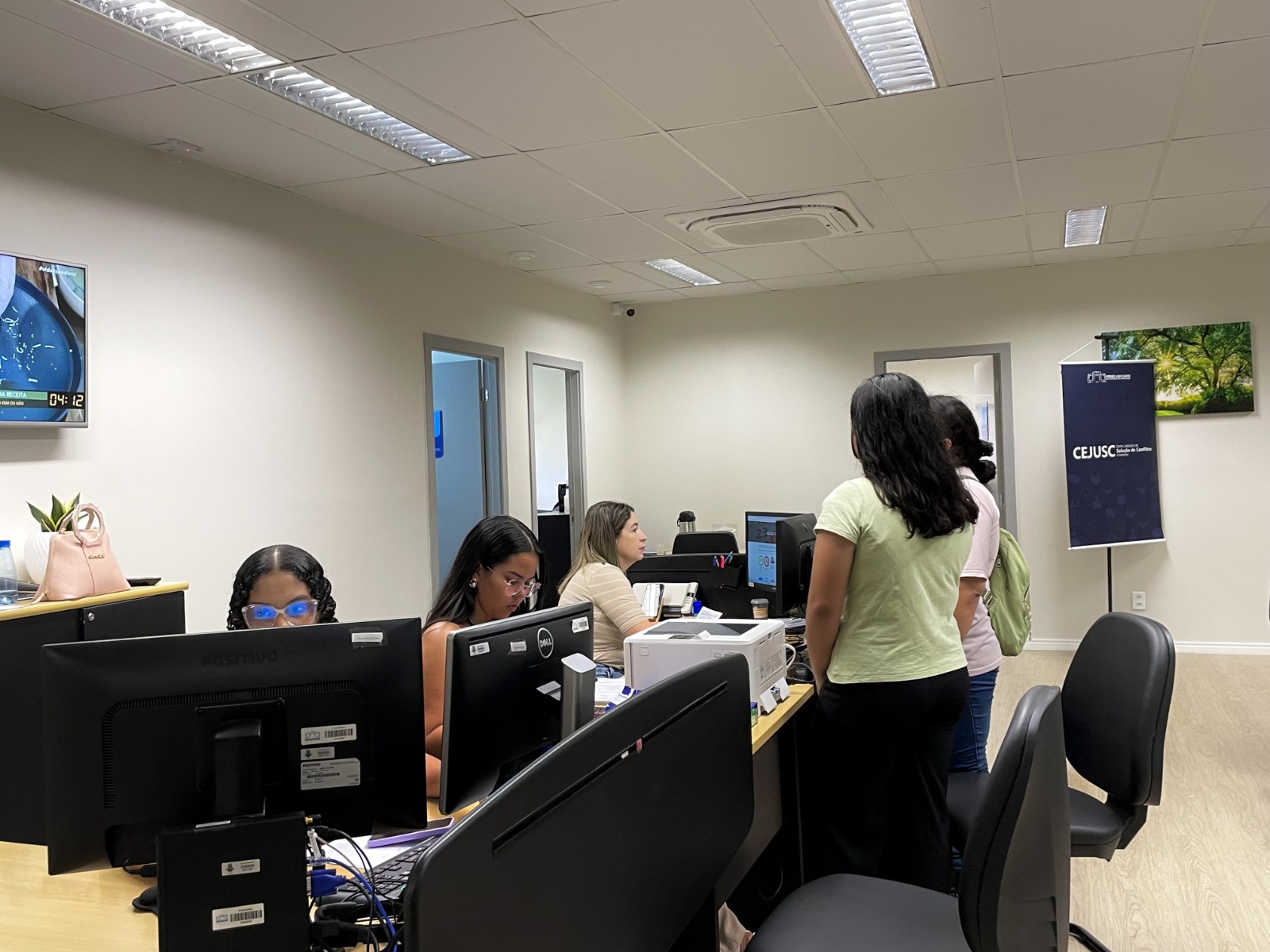 imagem colorida de duas mulheres em pé enfrente a uma mesa de atendimentos do CEJUS