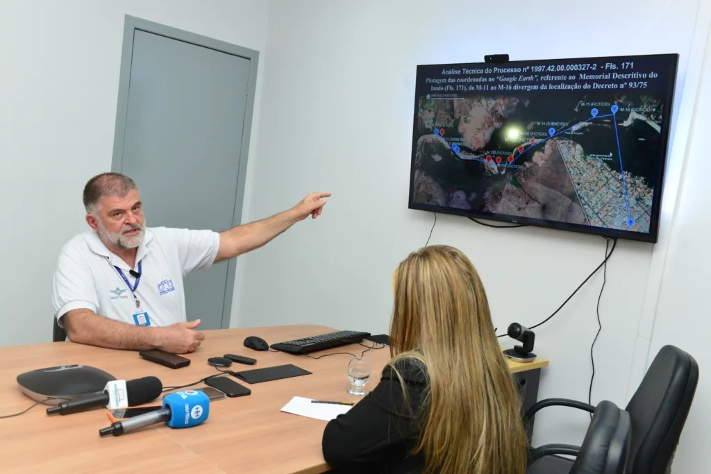 Homem explicando um mapa em uma tela para mulher sentada à mesa. Ambos estão em uma sala de reunião. Homem explicando um mapa em uma tela para mulher sentada à mesa. Ambos estão em uma sala de reunião.
