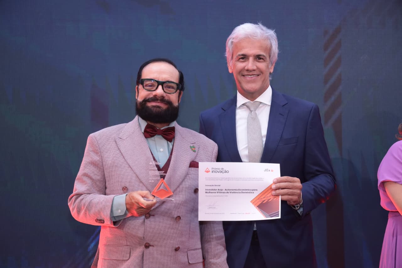 Foto colorida mostra o presidente do TJRR, desembargador Leonardo Cupello, segurando um troféu do Prêmio de Inovação J.Ex 2025, ao lado do juiz Jaime Plá, titular do 2º Juizado de Violência Doméstica e Familiar. O magistrado segura um certificado. Ambas conquistas das premiações dos projetos Intimajus e Investidor Anjo