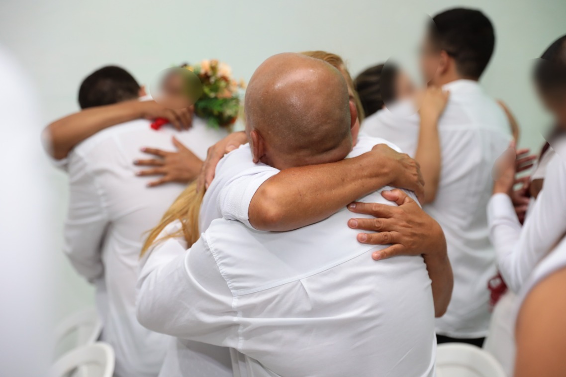 imagem em plano aberto mostrando vários casais se abraçando. Homens e mulheres se vestem de branco durante a cerimonia 