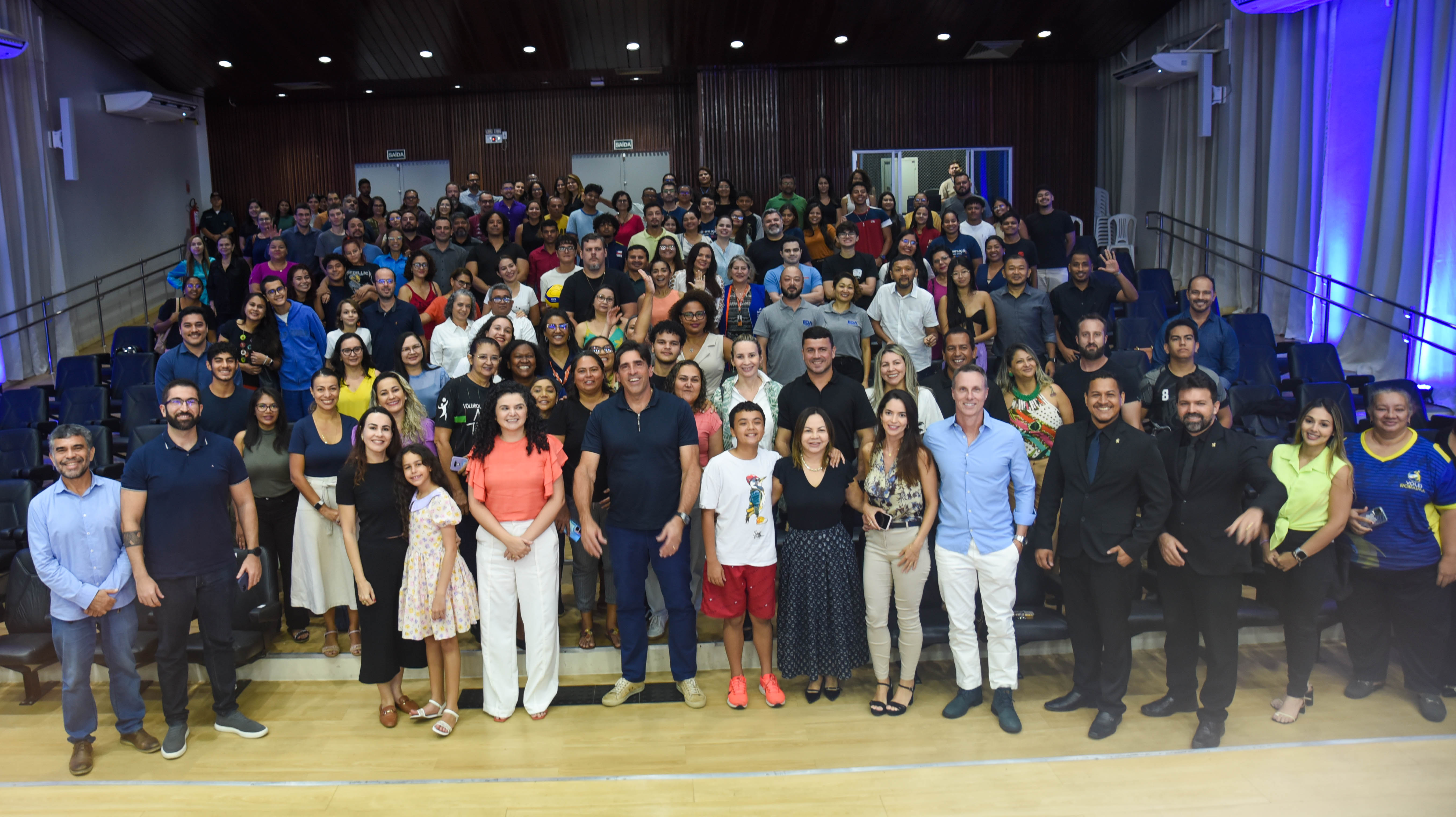 Foto colorida mostrando pessoas em pé, posando para foto, após a palestra no auditório do Fórum Civel