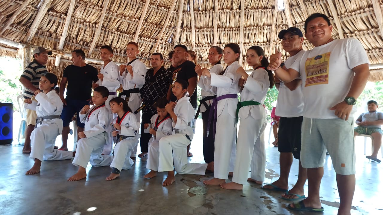  foto colorida de crianças indígenas e voluntários posando para a fotografia com roupas de karatê.