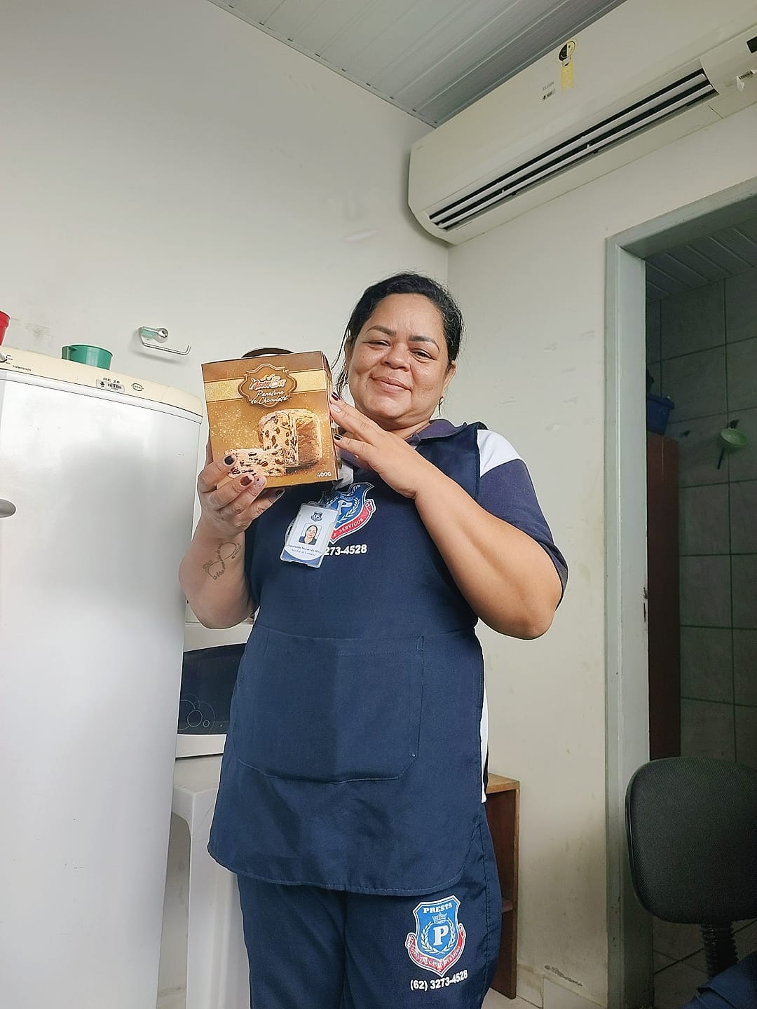 : foto colorida de uma servidora terceirizada posando para a fotografia com um panetone na mão.