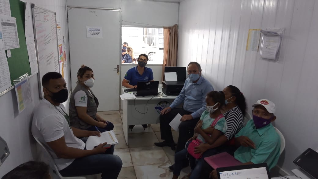 Servidora da Justiça Itinerante, sentada atrás de uma mesa, com pessoas sentadas em cadeiras de plástico na frente dela dentro de uma sala em um abrigo.