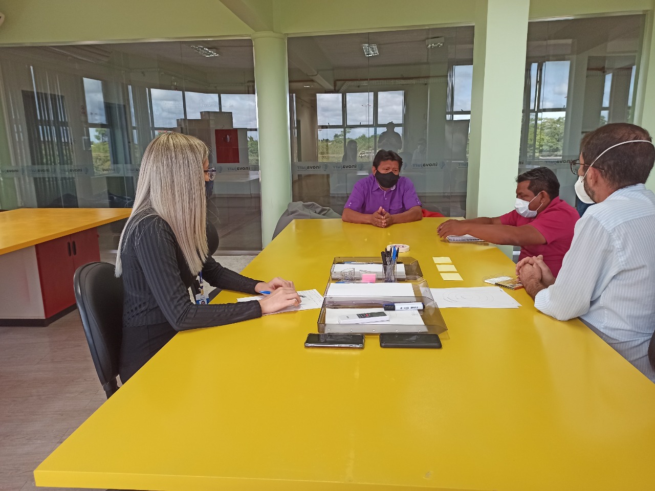 Equipe do tribunal de Justiça sentados ao redor de mesa de reuniões amarela, com Julio Macuxi.