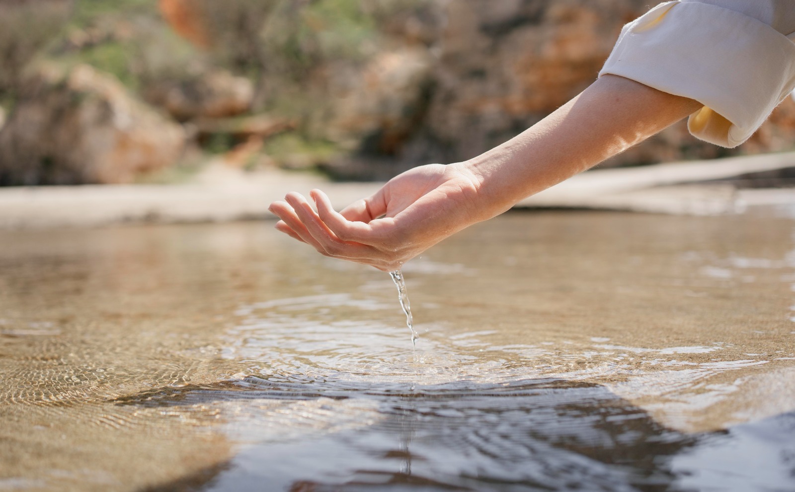 foto ilustrativa de uma mão pegando agua em um rio raso