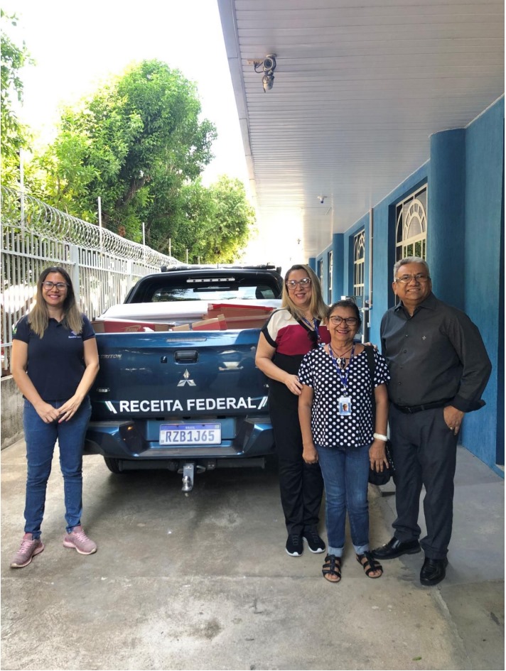 : Foto colorida mostra três mulheres e um homem posando para a foto ao lado de uma picape com a logo da Receita Federal