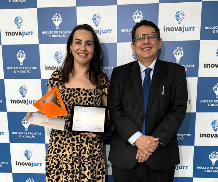 Foto colorida mostra o  presidente do Tribunal de Justiça de Roraima, desembargador Jésus Nascimento, posando para a foto ao lado da  coordenadora do Núcleo de Projetos e Inovação (NPI), Janaine Voltolini de Oliveira que segura uma placa de metal simbolizando o prêmio  de inovação 2023. 