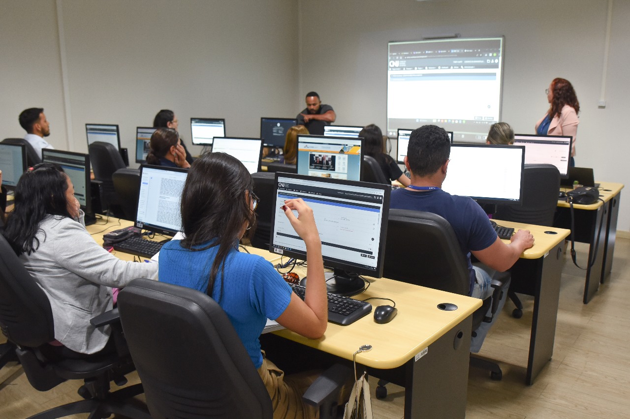 foto colorida de pessoas sentadas em mesas com computadores 