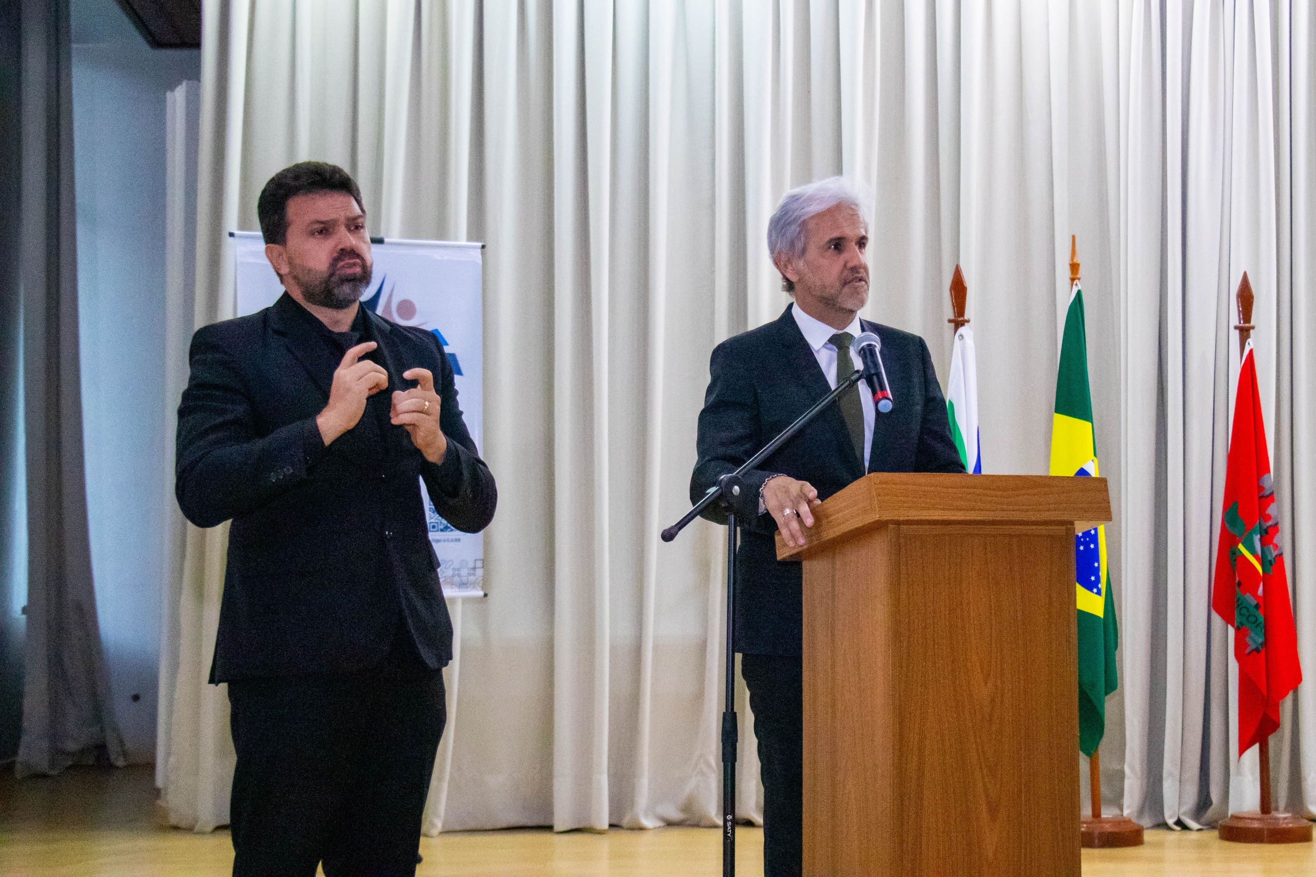 foto colorida do juiz titular do 2º Juizado de Violência Doméstica e Familiar, Jaime Plá Pujades falando no púlpito ao lado do interprete de libras 