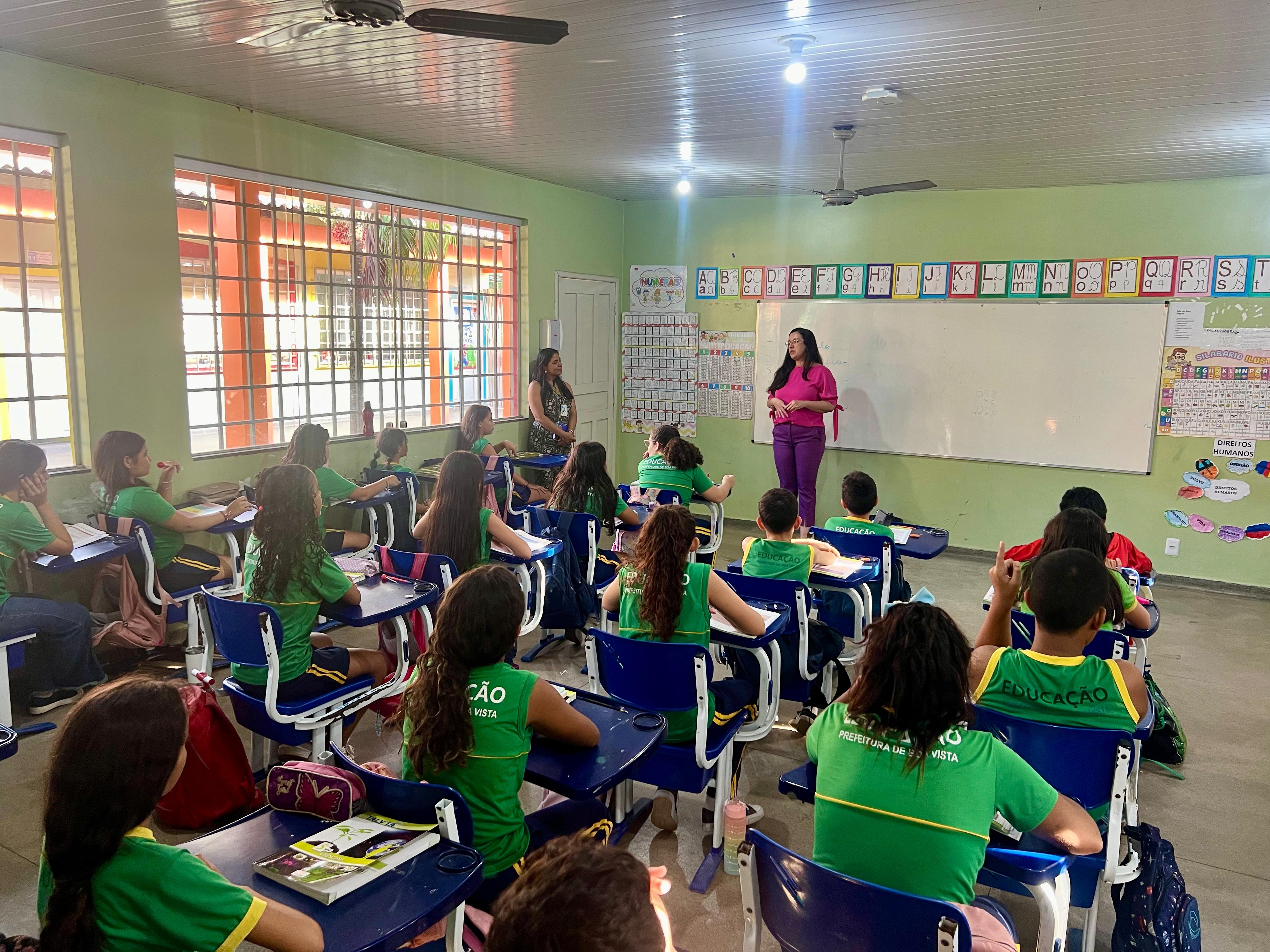 Foto colorida de crianças em sala de aula assistindo a uma palestra ministrada pela juíza Suelen Alves do TJRR. 