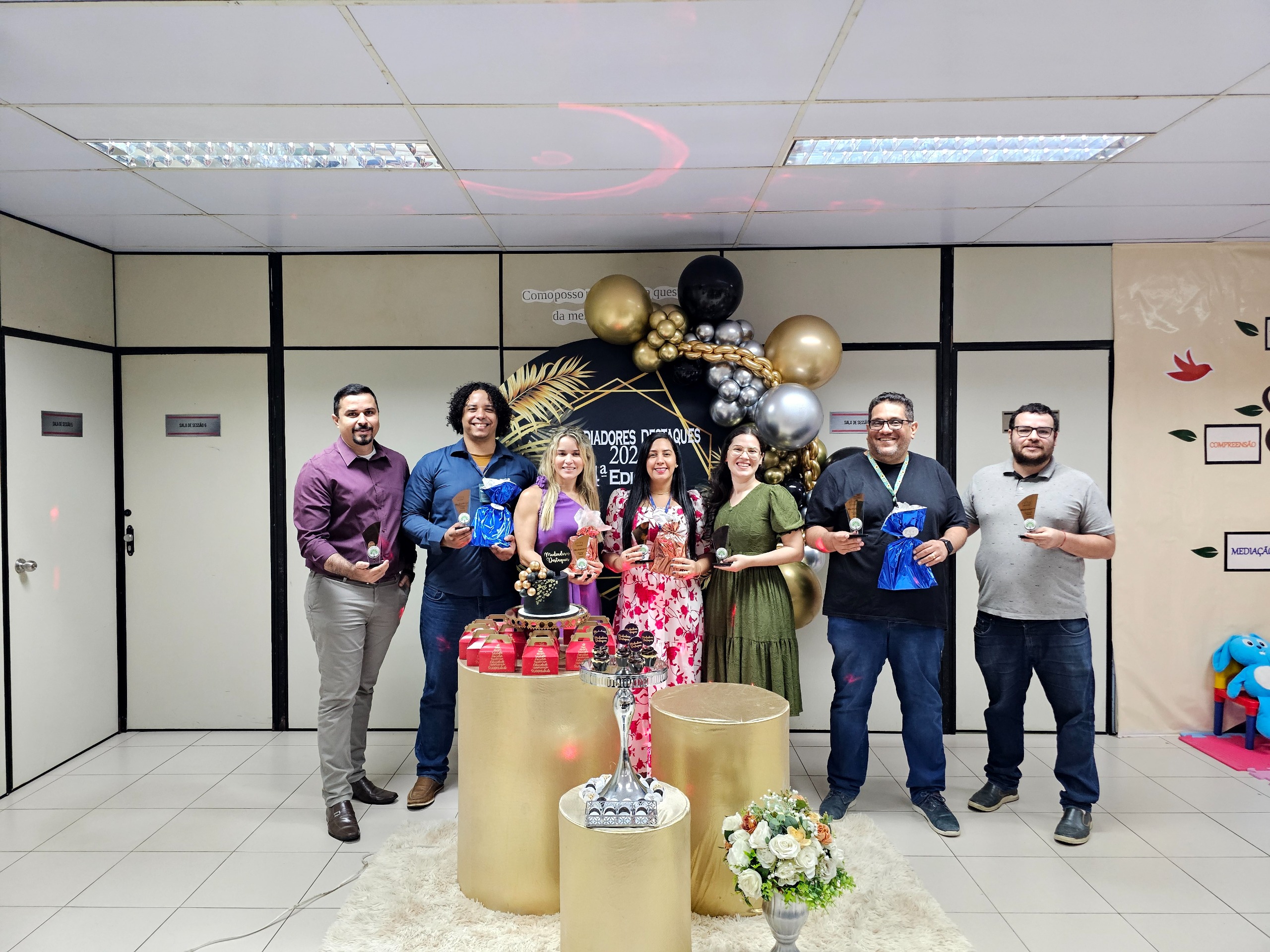 Imagem colorida mostra sete servidores premiados pelo NUPEMEC posando para foto com o prêmio.