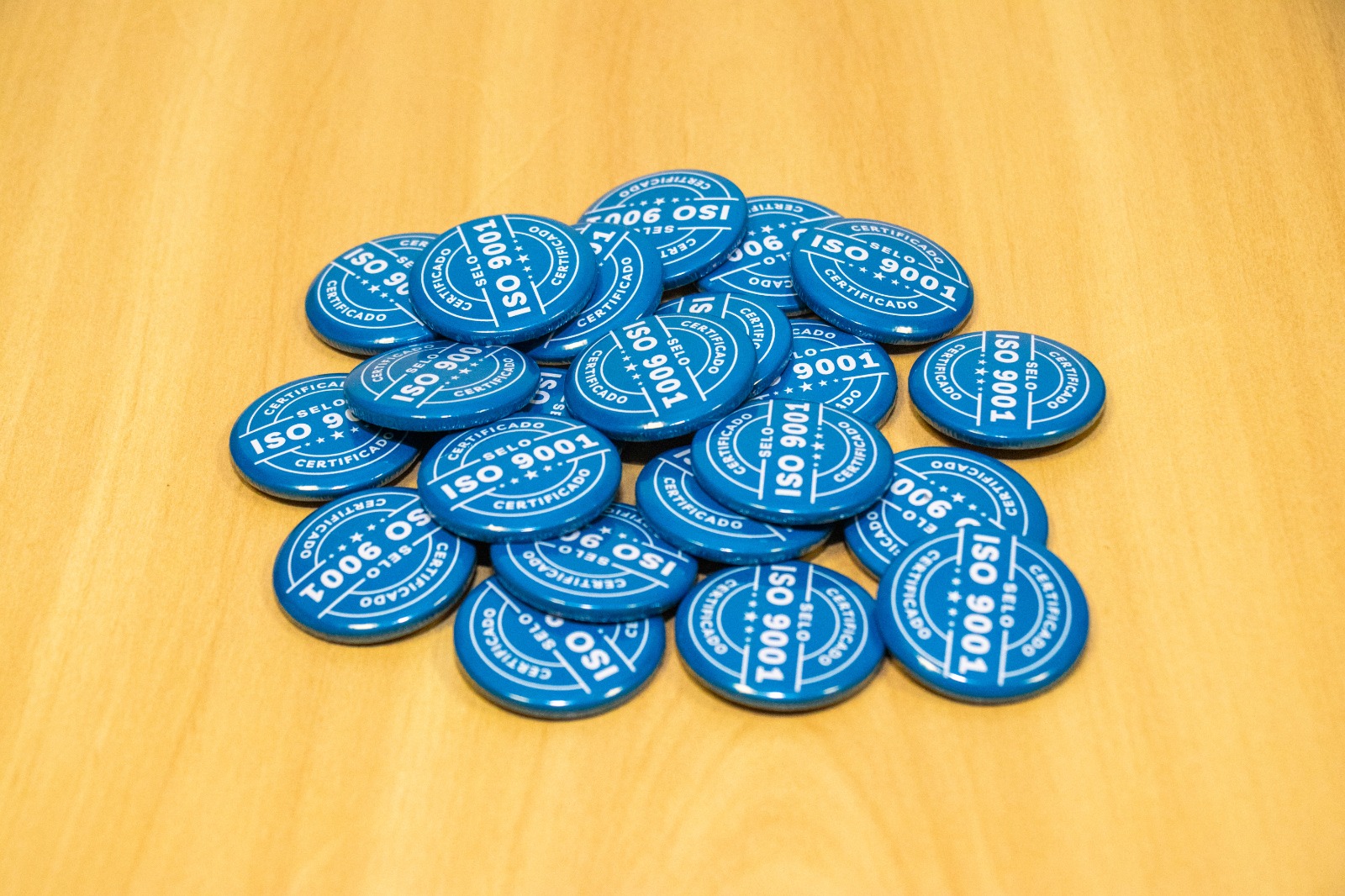  Imagem colorida mostra vários bottons com a certificação da ISO 9001. 