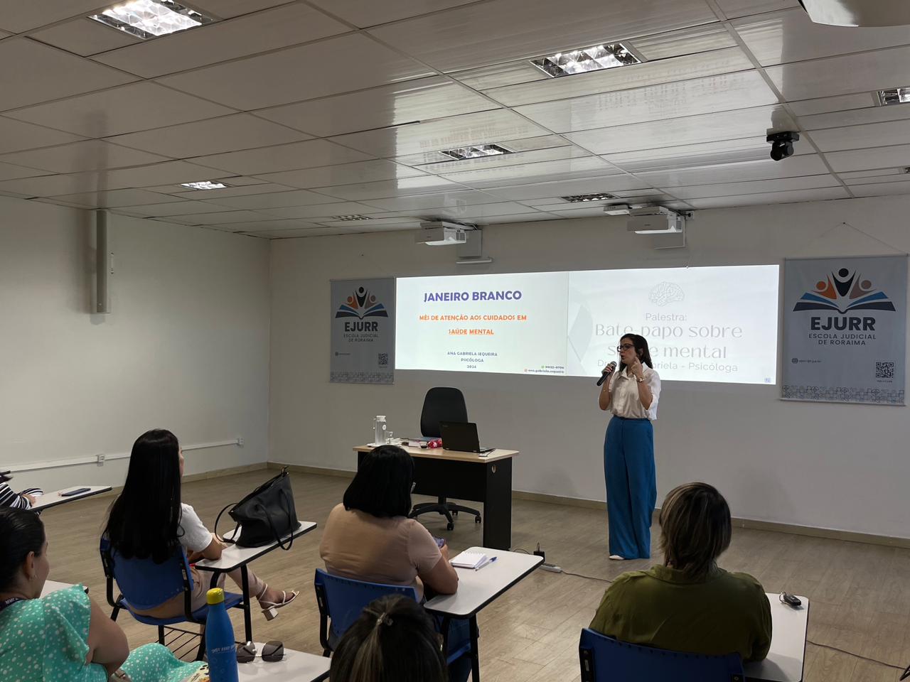 foto colorida de uma uma mulher palestrando para um turma de pessoas 