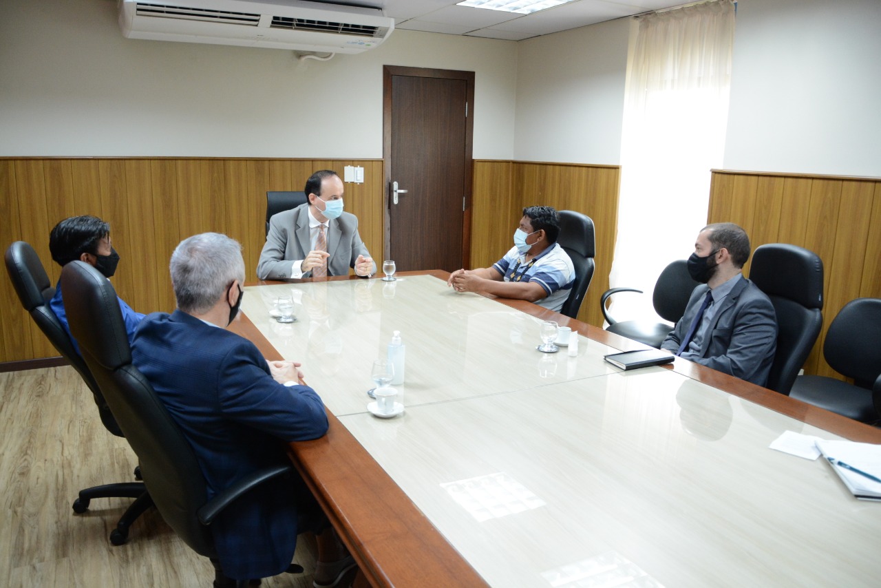 Presidente do Tribunal de Justiça, sentado em mesa de reuniões com servidores e com Aldenir Cadete, coordenador da região indígena Raposa Serra do Sol.