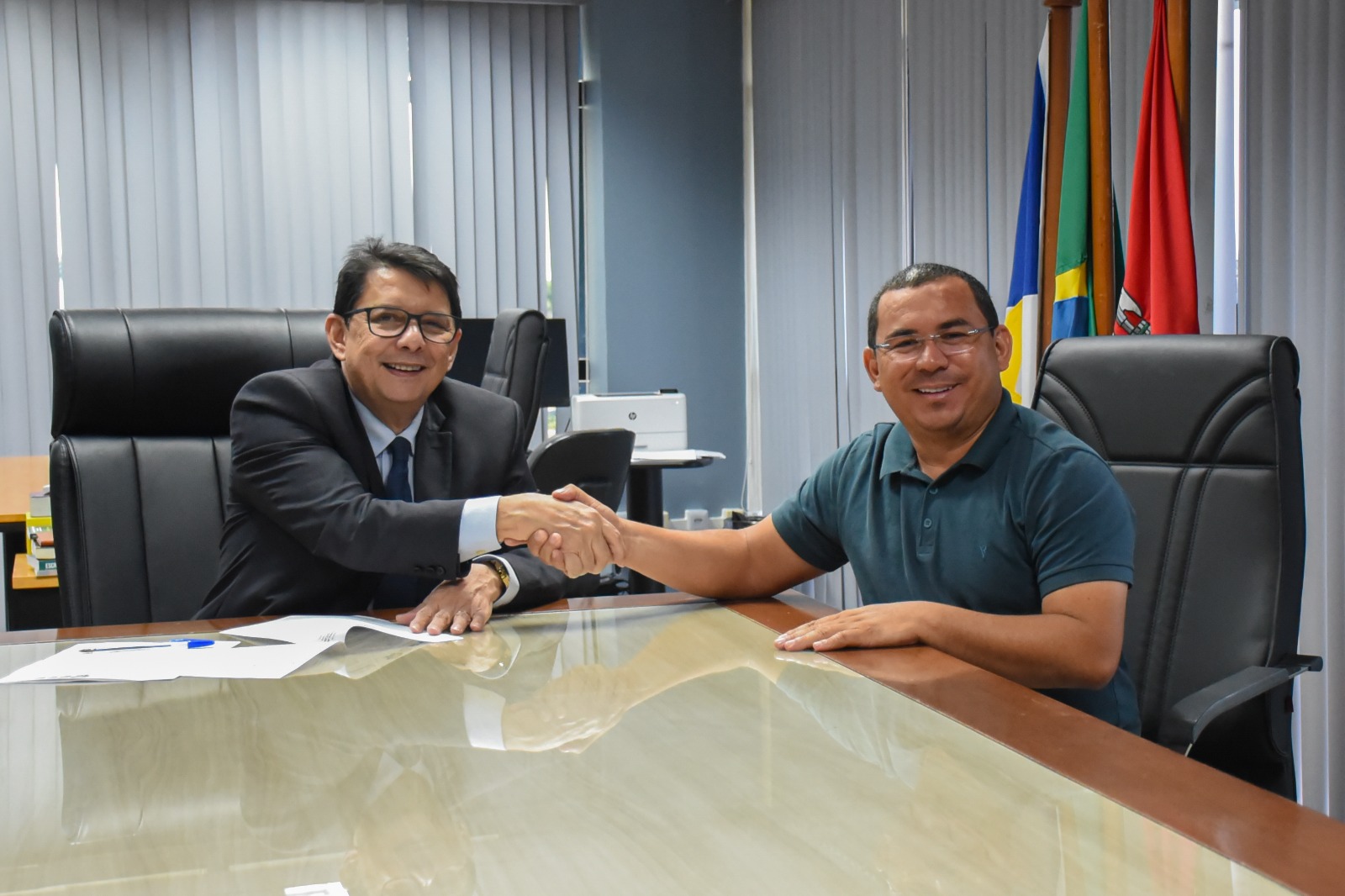 Foto colorida do presidente do Tribunal de Justiça de Roraima, Jésus Nascimento, apertando a mão do prefeito de Rorainópolis, Alessandro Daltro Sousa. Abaixo, está escrito: "PRECATÓRIOS - TJRR assina termo de compromisso com as prefeituras de Boa Vista e Rorainópolis ".