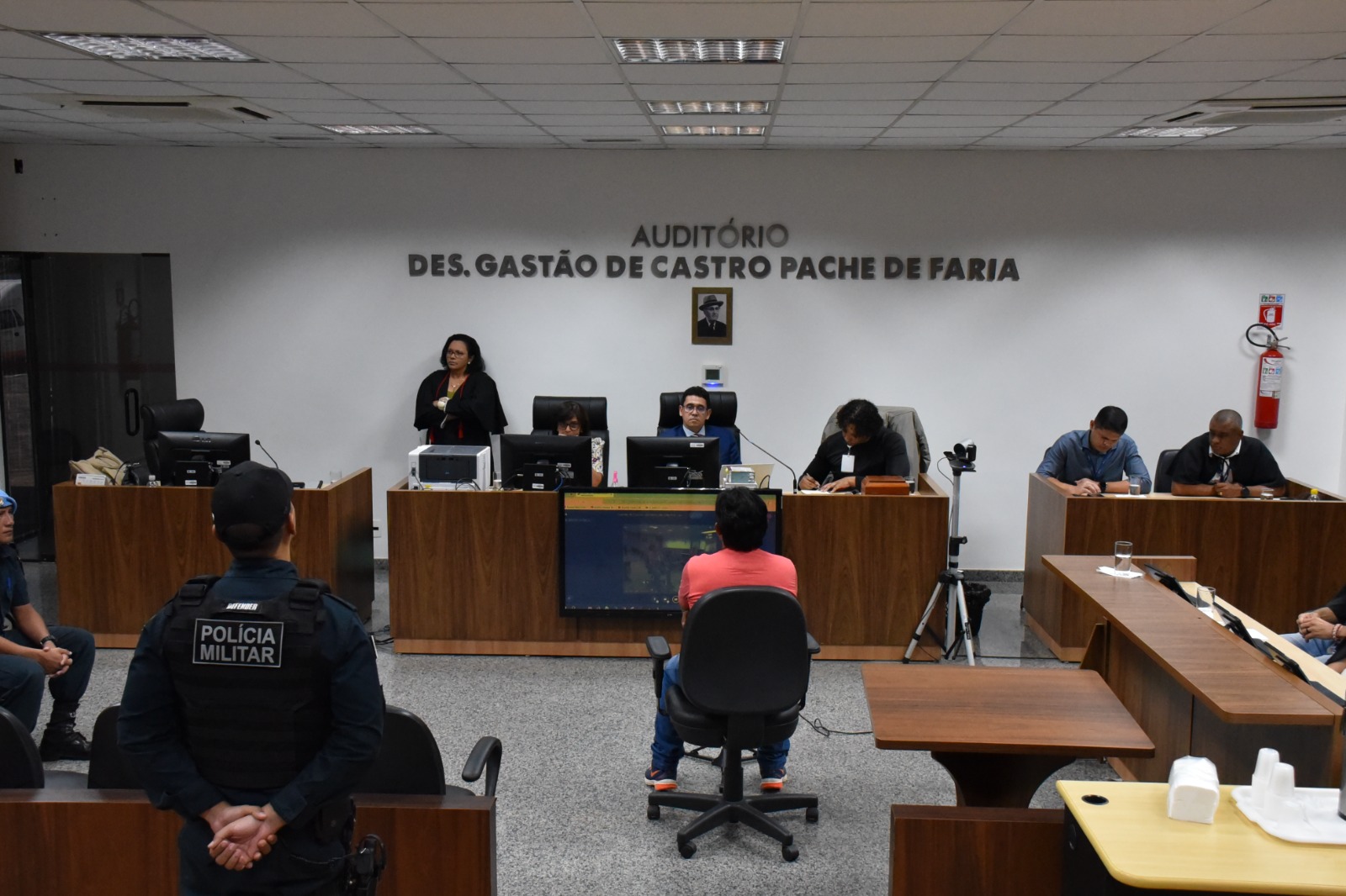 Imagem 1: Foto colorida de um audiório com uma pessoa sentada ao centro, de frente para outras que estão sentadas trabalhando. Abaixo, está escrito "PRIMEIRO SEMESTRE - Tribunal de Justiça de Roraima divulga pauta de júris e lista de jurados convocados"