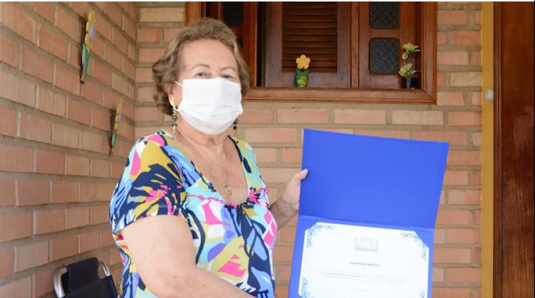 Foto de Dona Eleonora Silva de Morais segurando e mostrando seu certificado.