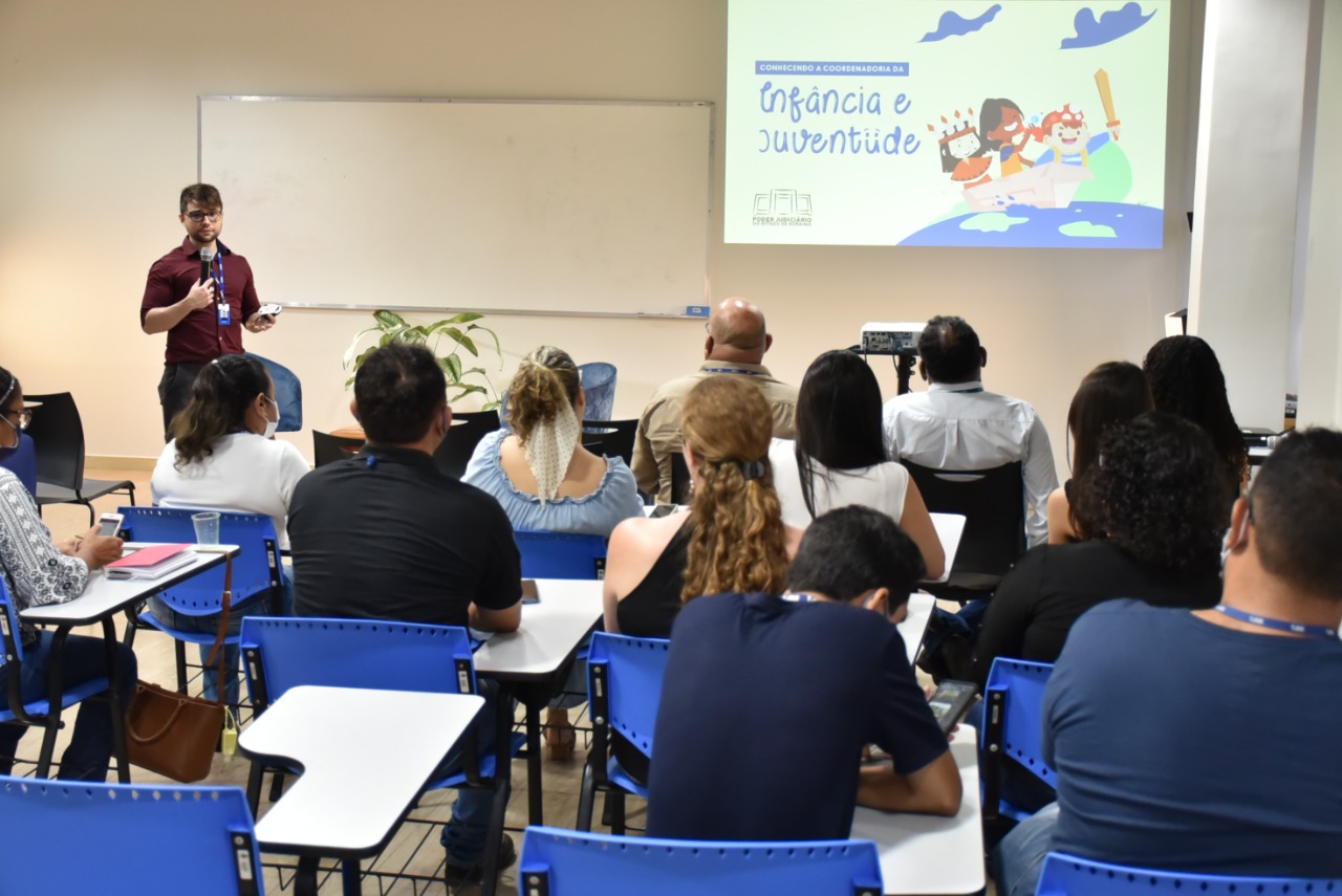 Imagem 2: Imagem colorida contém o servidor da Coordenadoria de Infância e Juventude, Josué Ferreira, palestrando no evento “Conhecendo a Coordenadoria da Infância e Juventude”, para servidores do TJRR sentados em frente dele assistindo a palestra. 