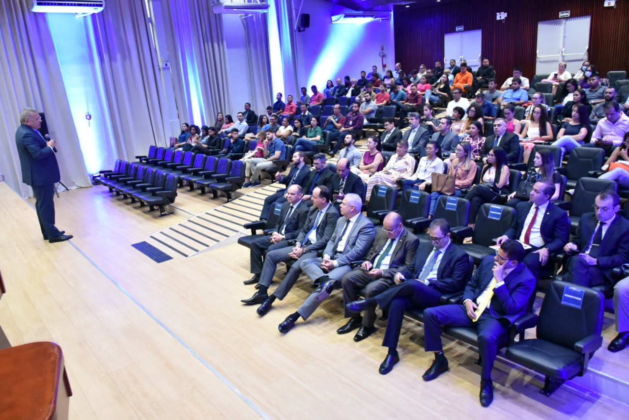 Imagem colorida mostra o auditório do Fórum Advogado Sobral Pinto com um público de magistrados, magistradas, servidores, servidoras, acadêmicos, assistindo a palestra realizada pelo o juiz presidente do Fórum Nacional da Mediação e Conciliação (Fonamec), Gildo Carvalho, que está em pé com o microfone na mão em frente ao público.