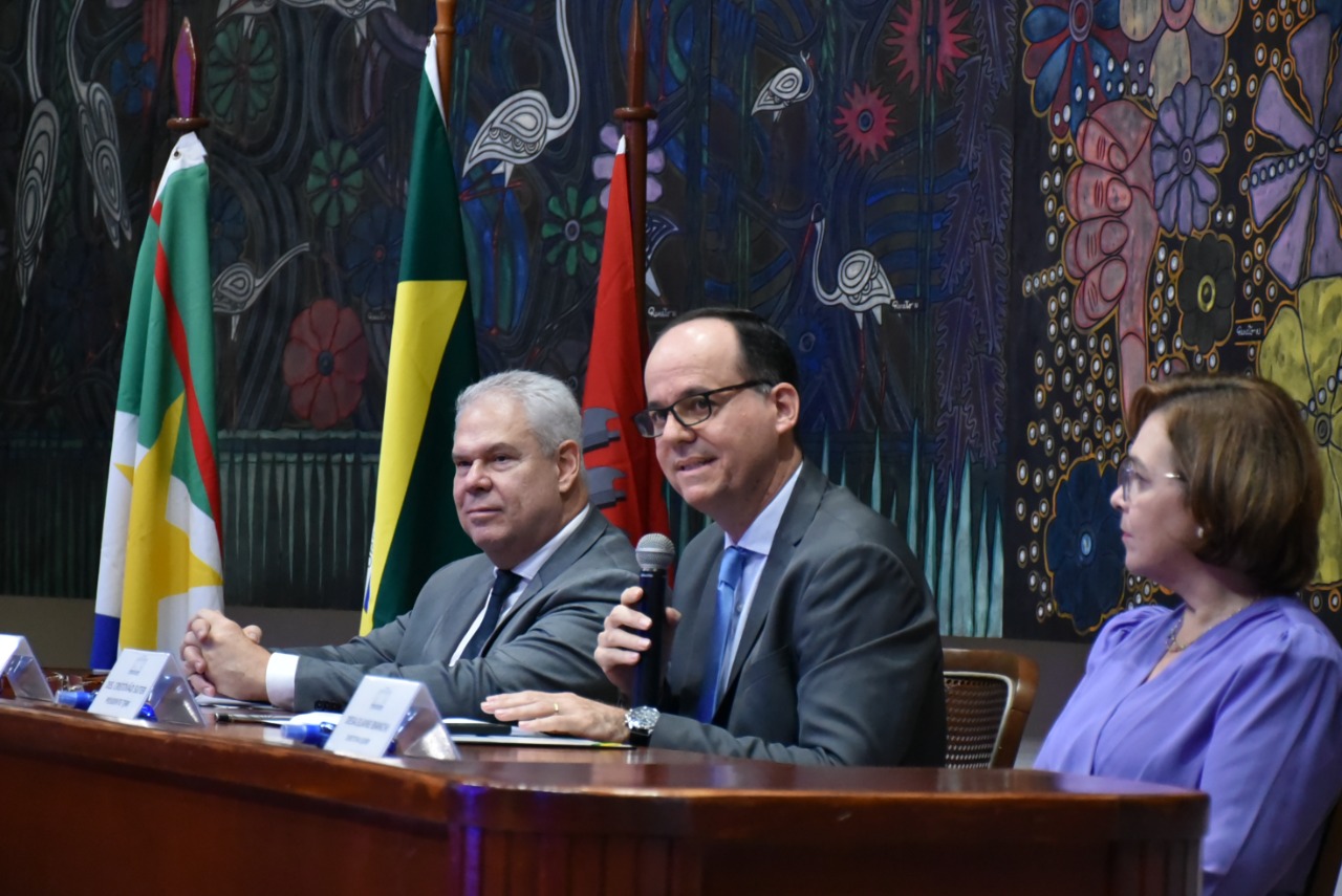 A imagem mostra o presidente, Desembargador Cristóvão Suter , o desembargador do Tribunal de Justiça de Pernambuco, Erik de Sousa Dantas e a desembargadora Elaine Bianchi, diretora da Ejurr, sentados atrás de uma bancada. O Presidente está entre os dois magistrados discursando com o microfone na mão. 