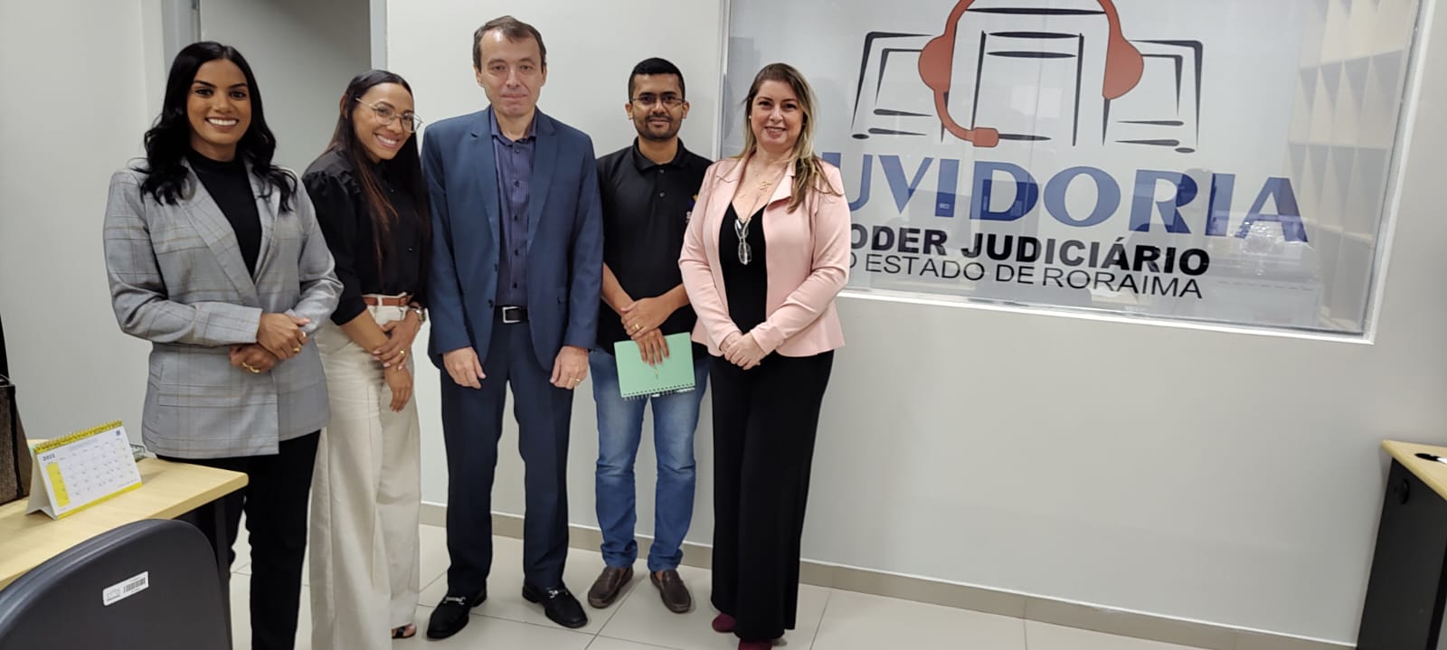 Imagem colorida mostra o ouvidor-geral do Tribunal de Justiça de Roraima (TJRR), desembargador Erick Linhares em pé, posando para a foto, ao lado dos representantes de órgãos de defesa do consumidor. Ao fundo a placa da ouvidoria do poder judiciario.