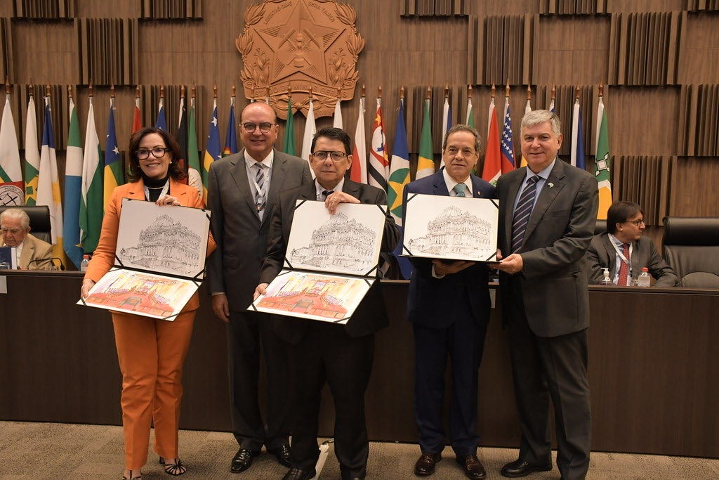 Imagem colorida mostra o presidente do Tribunal de Justiça de Roraima (TJRR), desembargador Jésus Nascimento, ao lado do presidente do TJMG, desembargador José Arthur de Carvalho Pereira Filho, a assessora técnica especializada do TJMG, Tatiana Camarão, o desembargador do TJMG José Marcos Rodrigues Vieira, diretor executivo de Finanças e Gestão Orçamentária do TJMG, Eduardo Antônio Codo Santos, segurando duas  gravuras criadas pelo desembargador mineiro José Marcos Rodrigues Vieira.