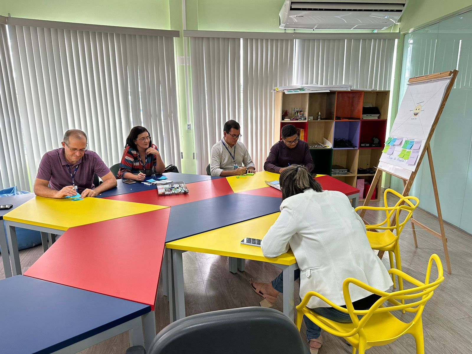 foto colorida de servidores do fórum sentados à nessa colorida escrevendo em papeis de cor 