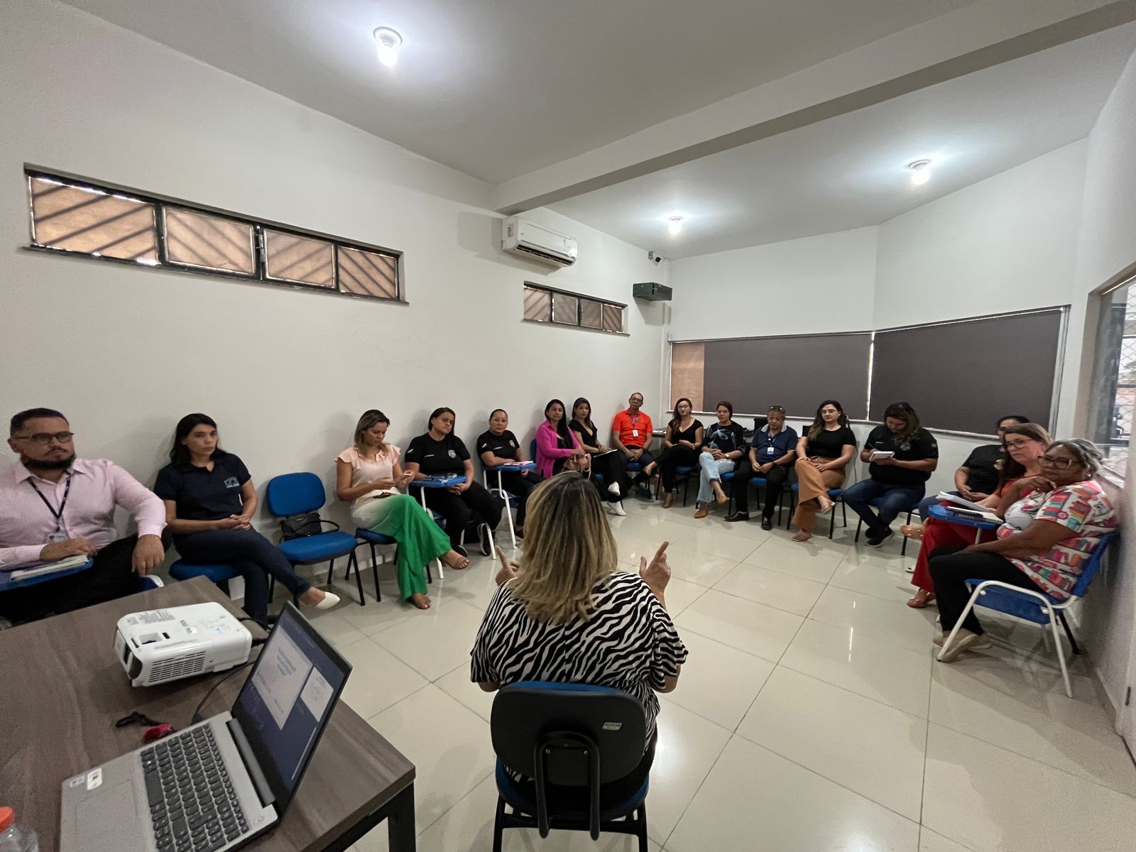 foto colorida de uma mulher rodeada por pessoas uma turma de pessoas sentadas em cadeiras 