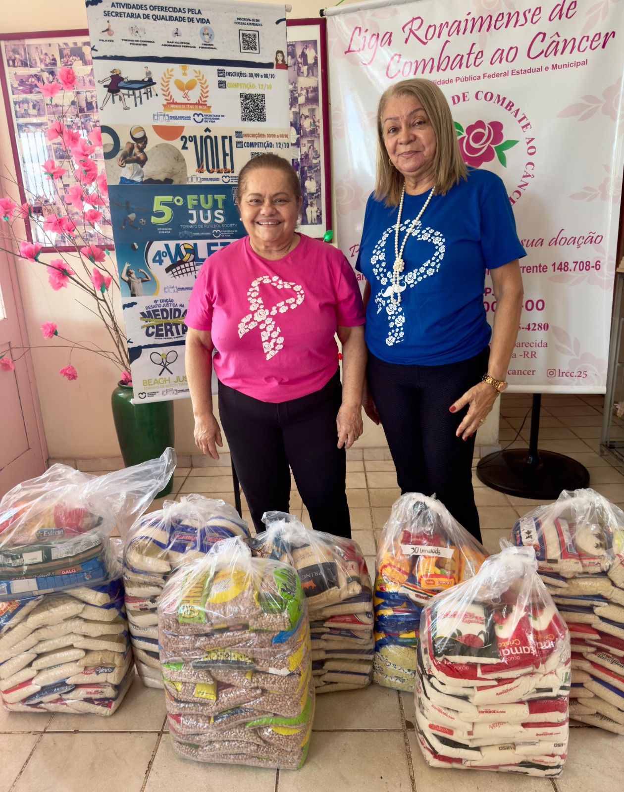 foto colorida mostra duas pessoas em pé posando para a foto com a doação de alimentos