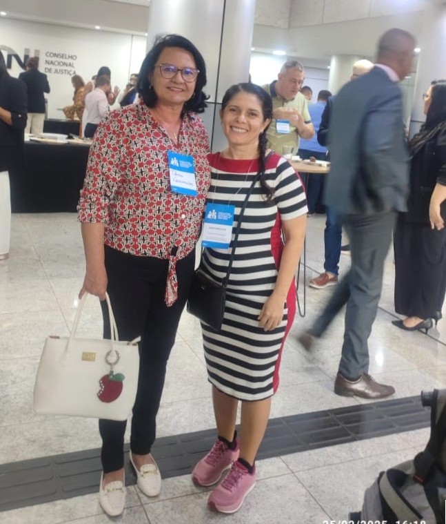 Imagem colorida mostra a Desembargadora Tânia Vasconcellos e a servidora Claudete Pereira,participantes do evento posando para uma foto no saguão do Conselho Nacional de Justiça (CNJ), Ambas utilizam crachás de identificação e sorriem para a câmera. No ambiente, há outras pessoas circulando e interagindo. Ao fundo, o nome do Conselho Nacional de Justiça está visível na parede. Imagem colorida mostra a Desembargadora Tânia Vasconcellos e a servidora Claudete Pereira,participantes do evento posando para uma foto no saguão do Conselho Nacional de Justiça (CNJ), Ambas utilizam crachás de identificação e sorriem para a câmera. No ambiente, há outras pessoas circulando e interagindo. Ao fundo, o nome do Conselho Nacional de Justiça está visível na parede.