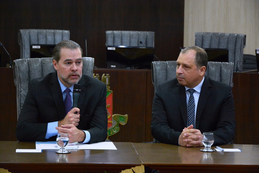 Ministro Dias Toffoli e desembargador Mozarildo Cavalcanti, sentados à uma mesa de madeira, no pleno do Tribunal de Justiça de Roraima, no momento em que Toffoli faz uso da palavra  