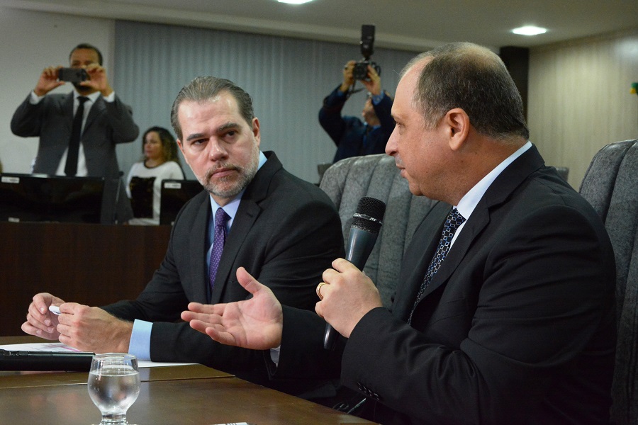 Ministro Dias Toffoli e desembargador Mozarildo Cavalcanti, sentados à uma mesa de madeira, no pleno do Tribunal de Justiça de Roraima, no momento em que o desembargador Mozarildo faz uso da palavra  