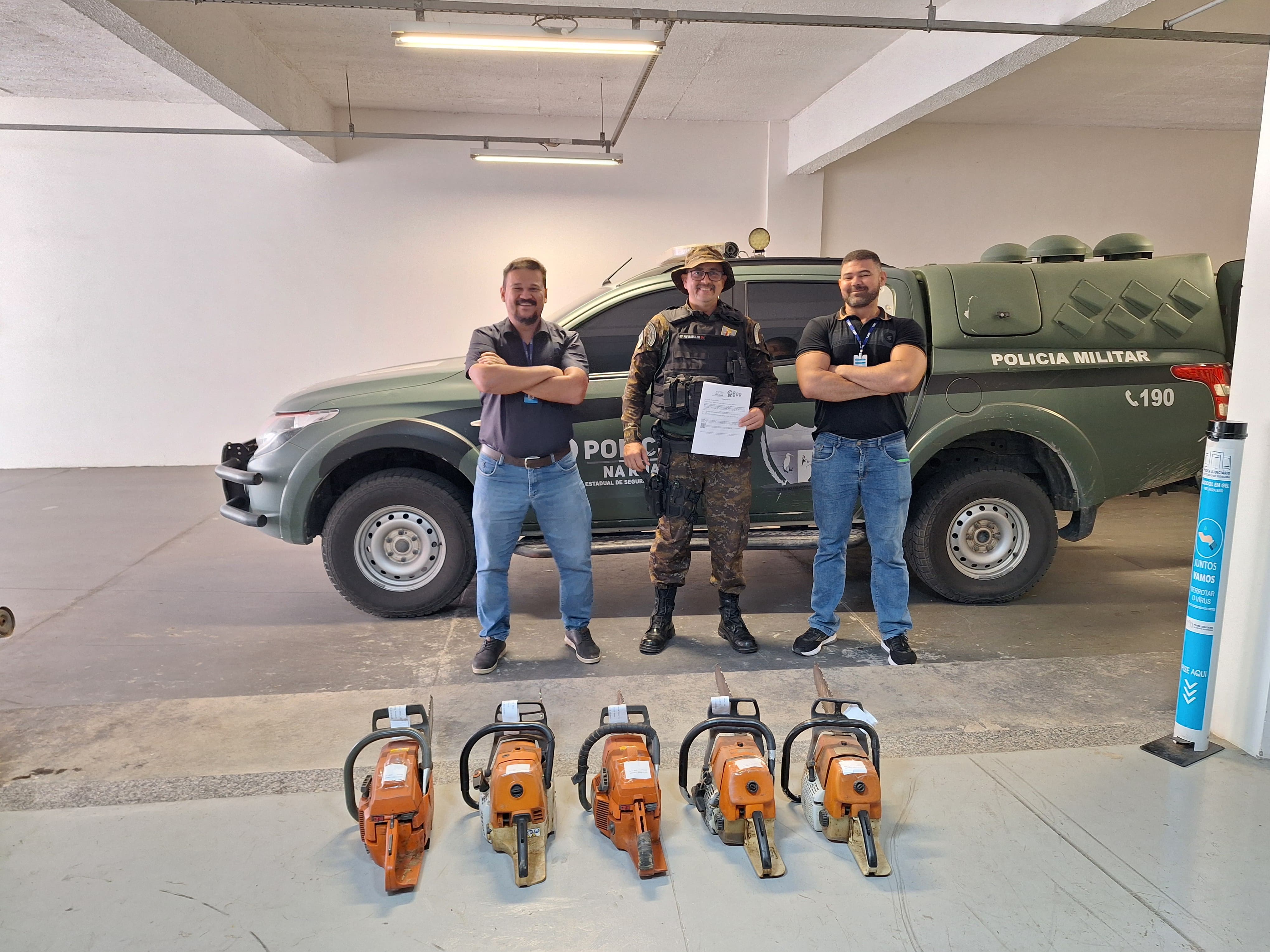 foto colorida de 2 servidores do TJRR e um a agente pousando para foto durante a doação de cinco motosserras à Companhia Independente de Policiamento Ambiental (CIPA). A